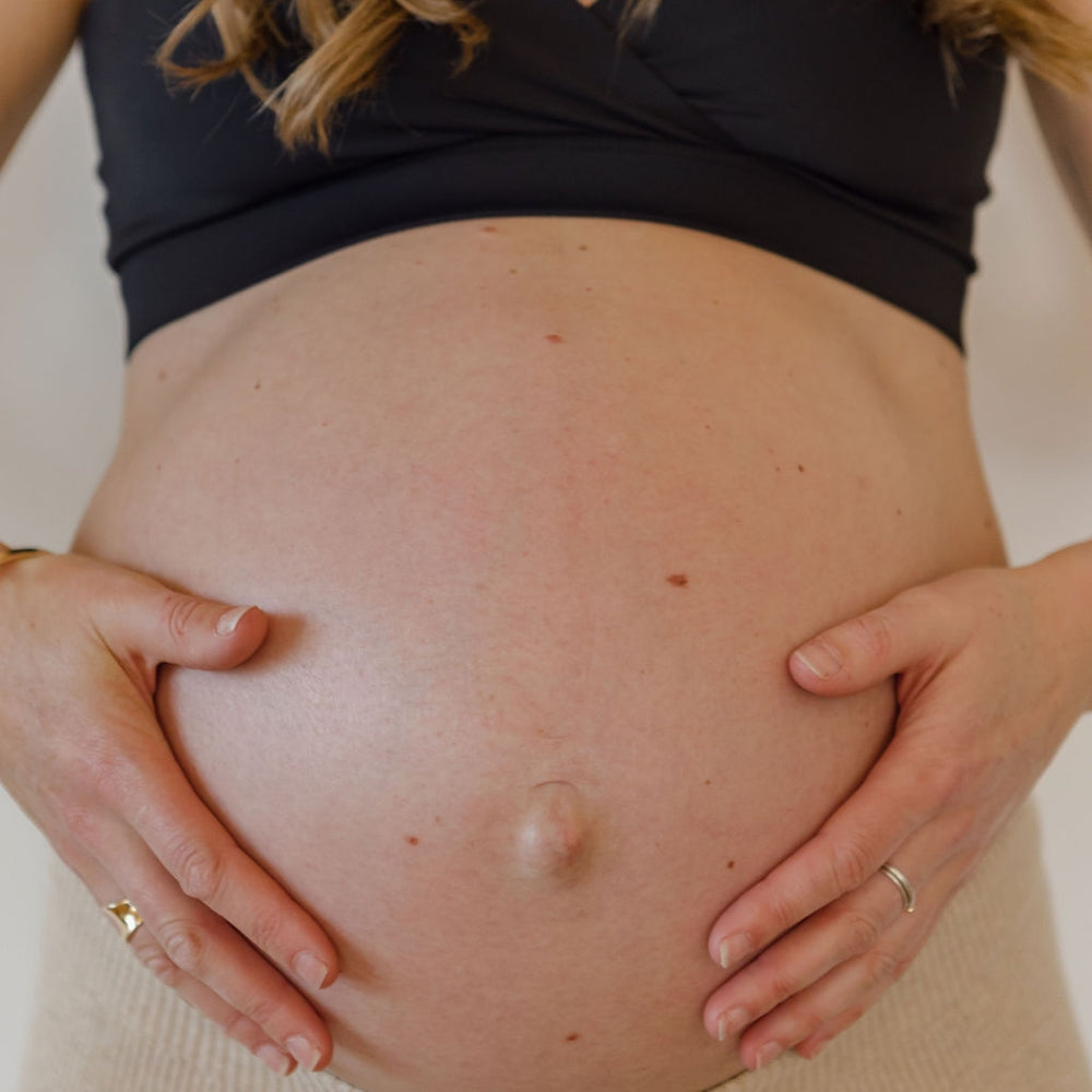 A mid shot of a woman preparing for birth. She is wearing a maternity bra and facing her bare pregnant stomach to the camera.
