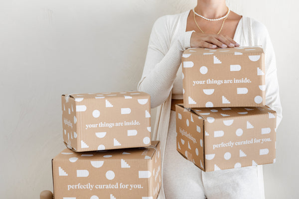 A person holds three cardboard boxes with text; the top reads "your things are inside," and the bottom "perfectly curated for you.