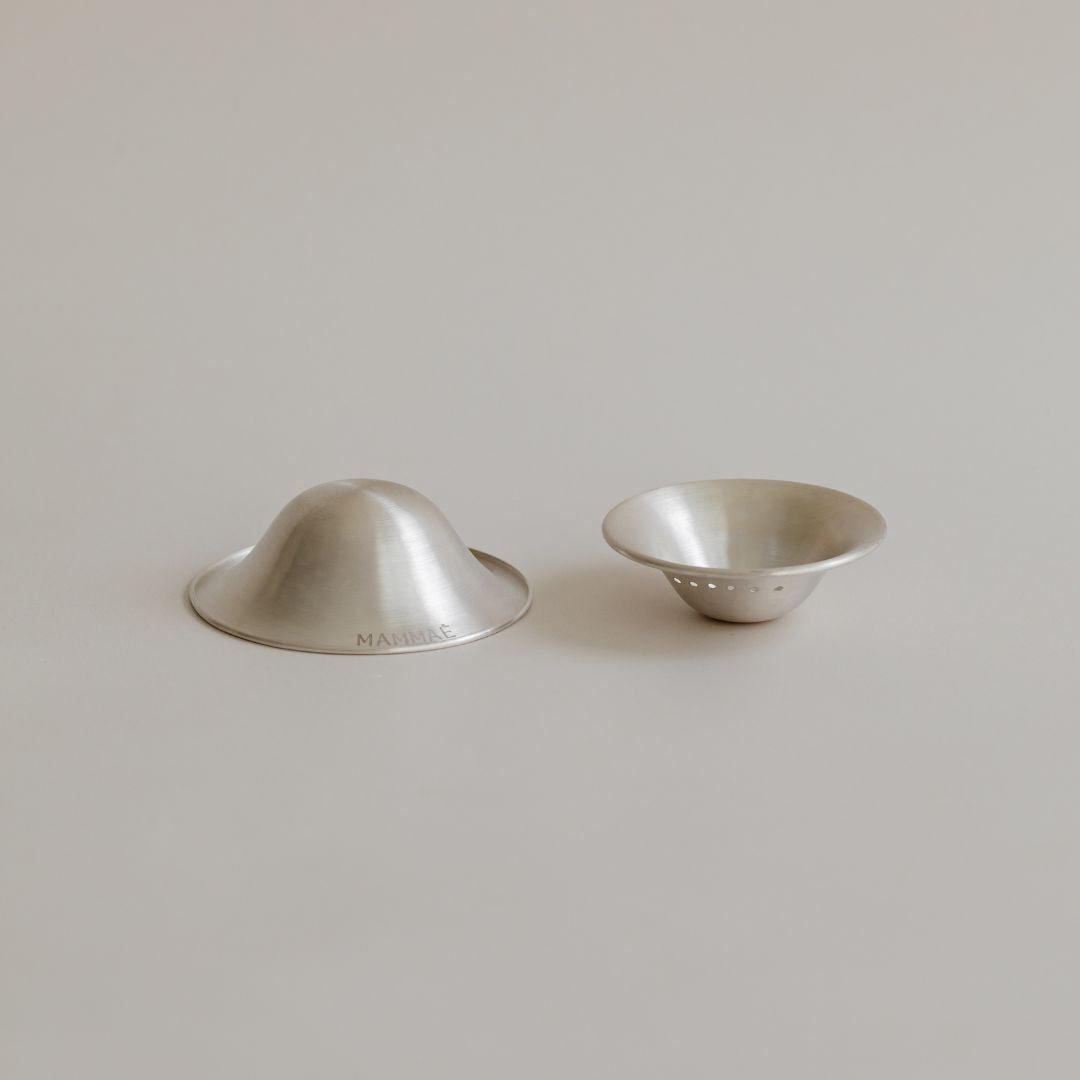 Two metal bowls on a light background, one inverted and one upright, both with a brushed finish. These are Mammae fine silver nipple cups.