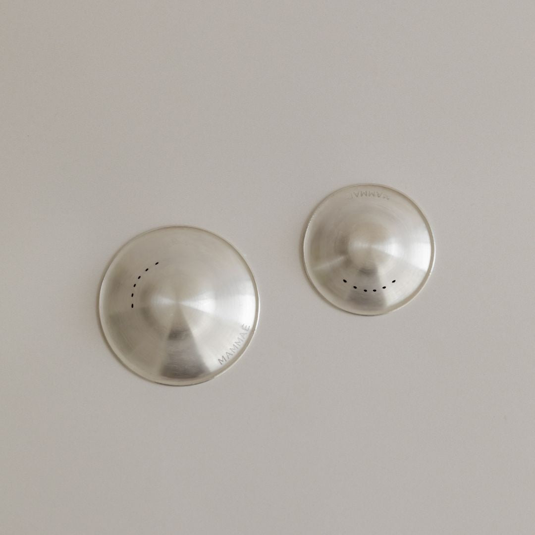 Two Mammae silver nipple cups on a natural light-colored surface.