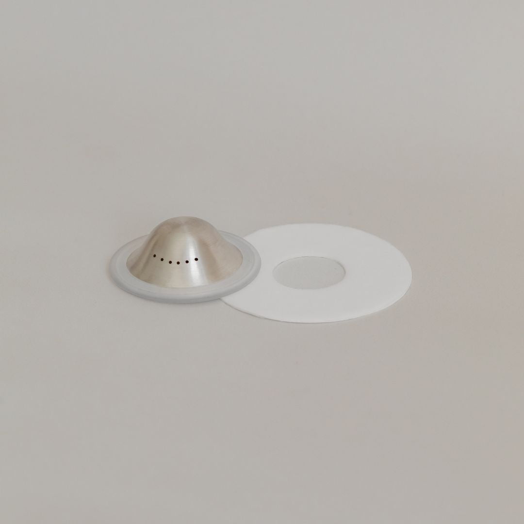 A Mammae silver nipple care bundle beside its white circular paper filter on a neutral background.