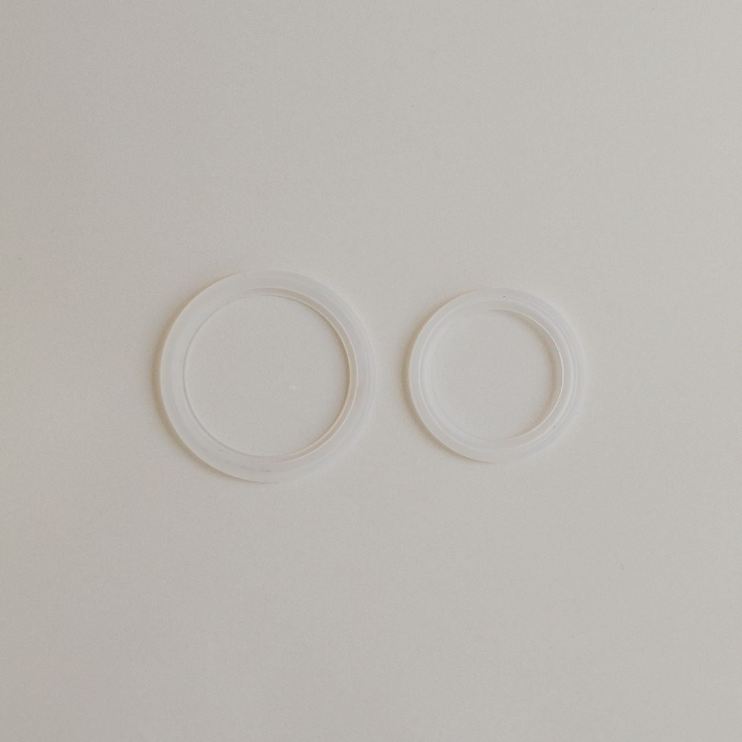 Two white circular rings positioned side by side on a neutral background, resembling fine Mammae silver nipple cups.