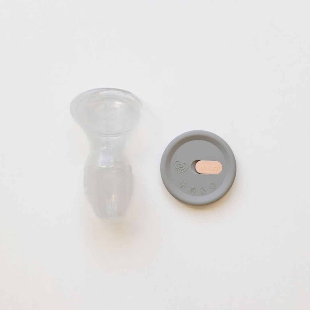A small Haakaa Silicone Breast Pump & Silicone Cap Gen 1 bottle with a lid sitting on a white surface.