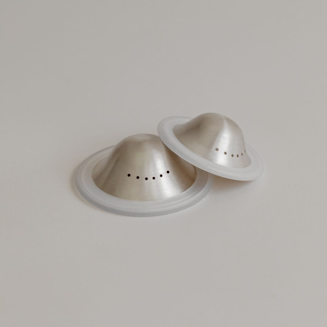 Two fine Mammae silver nipple cups on a light grey background.