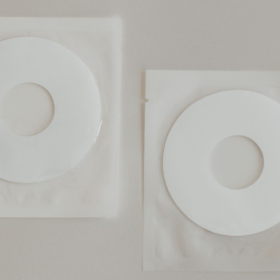 Two white circular Mammae silver nipple care pads with central holes, placed on square translucent sheets, set against a neutral background.