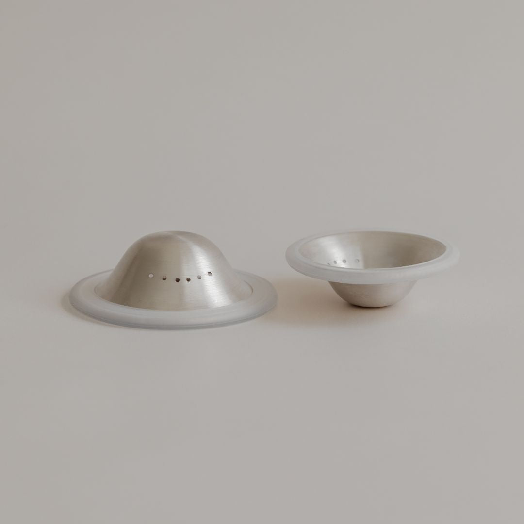 Two fine Mammae silver nipple cups, one dome-shaped and one bowl-shaped, on a light grey background.