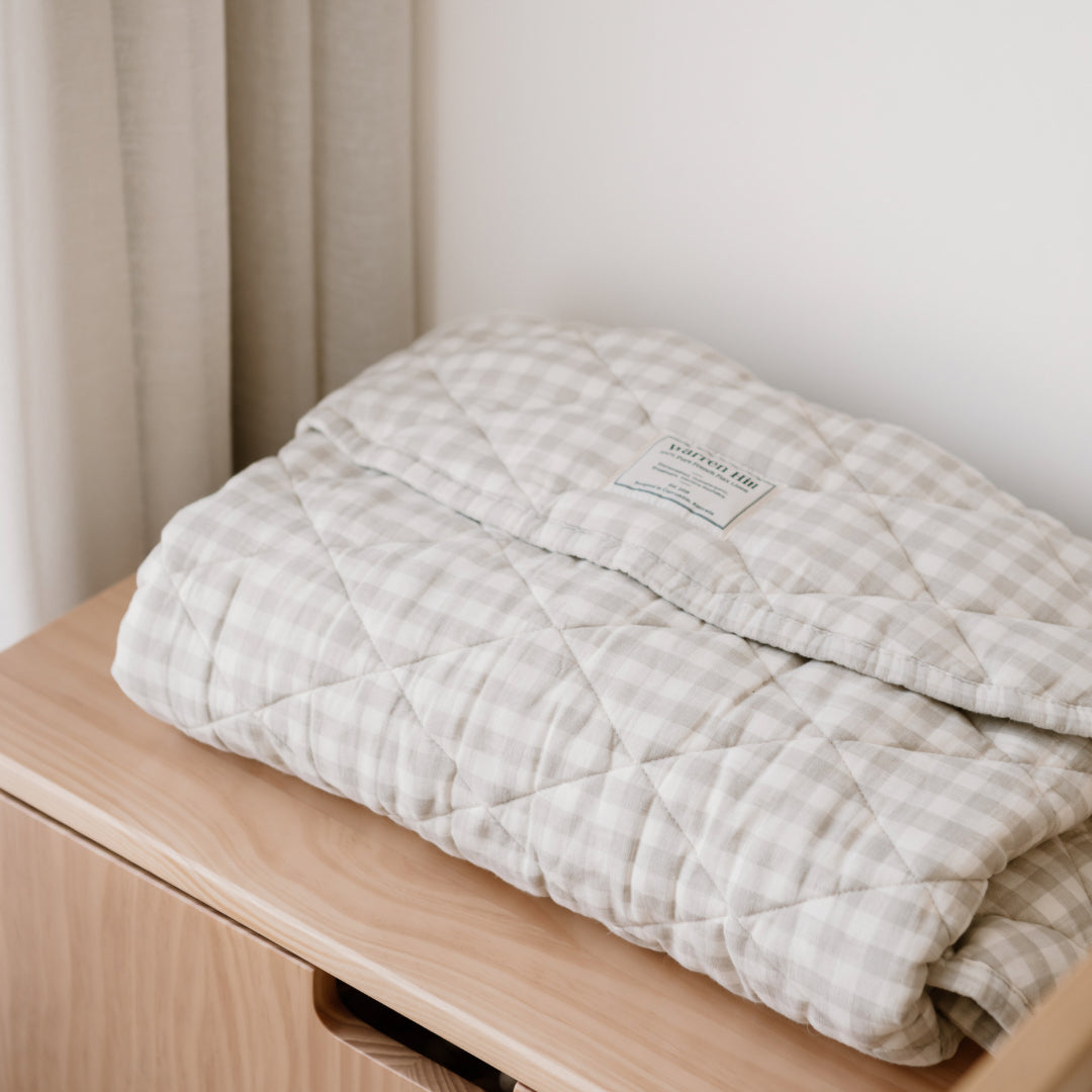 Folded Warren Hill gingham hypoallergenic baby play mat on a wooden table against a neutral background.
