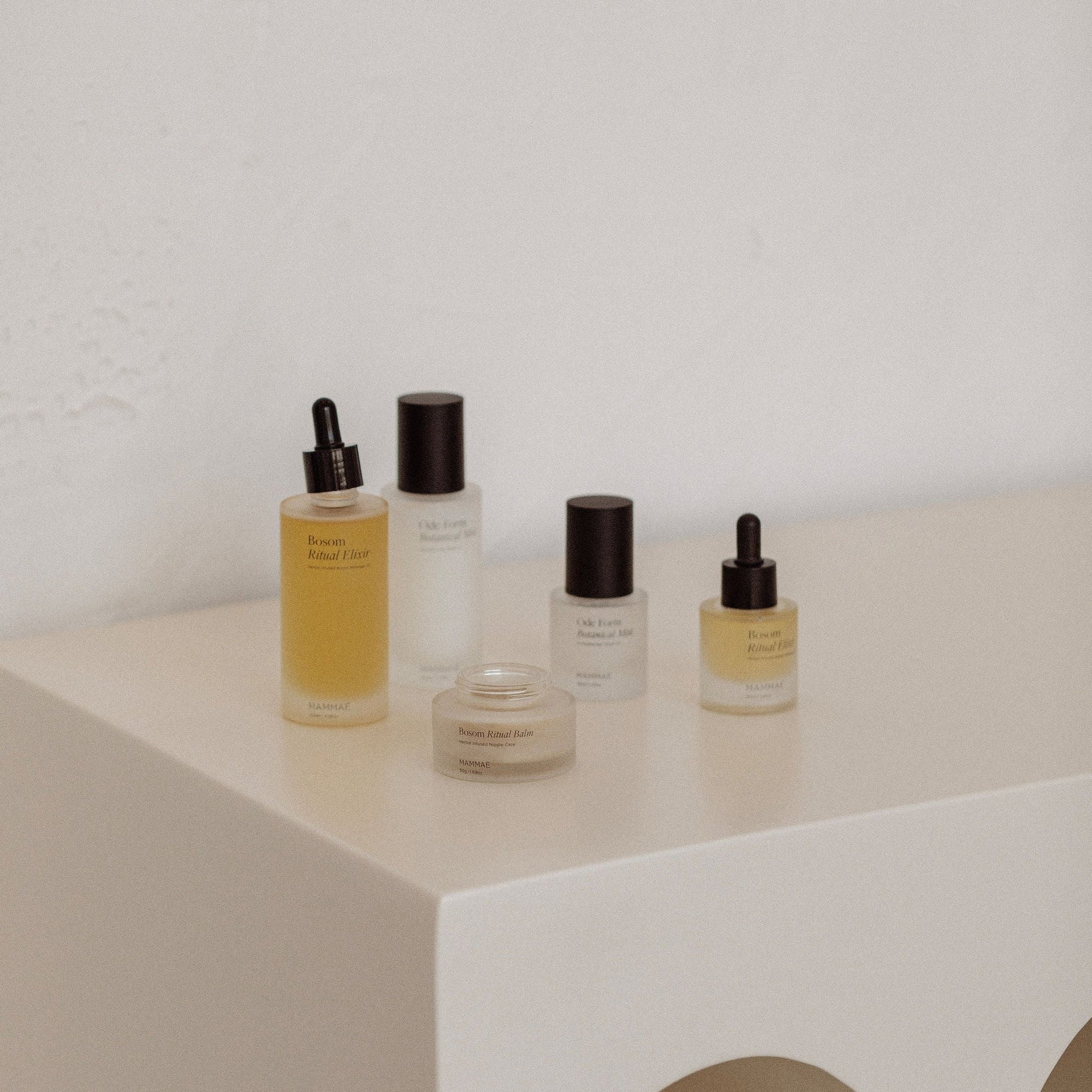 A white table with several cosmetic products, including an EXCLUSIVE Mini Bosom Ritual Elixir, highlighting breast health awareness by Mammae.