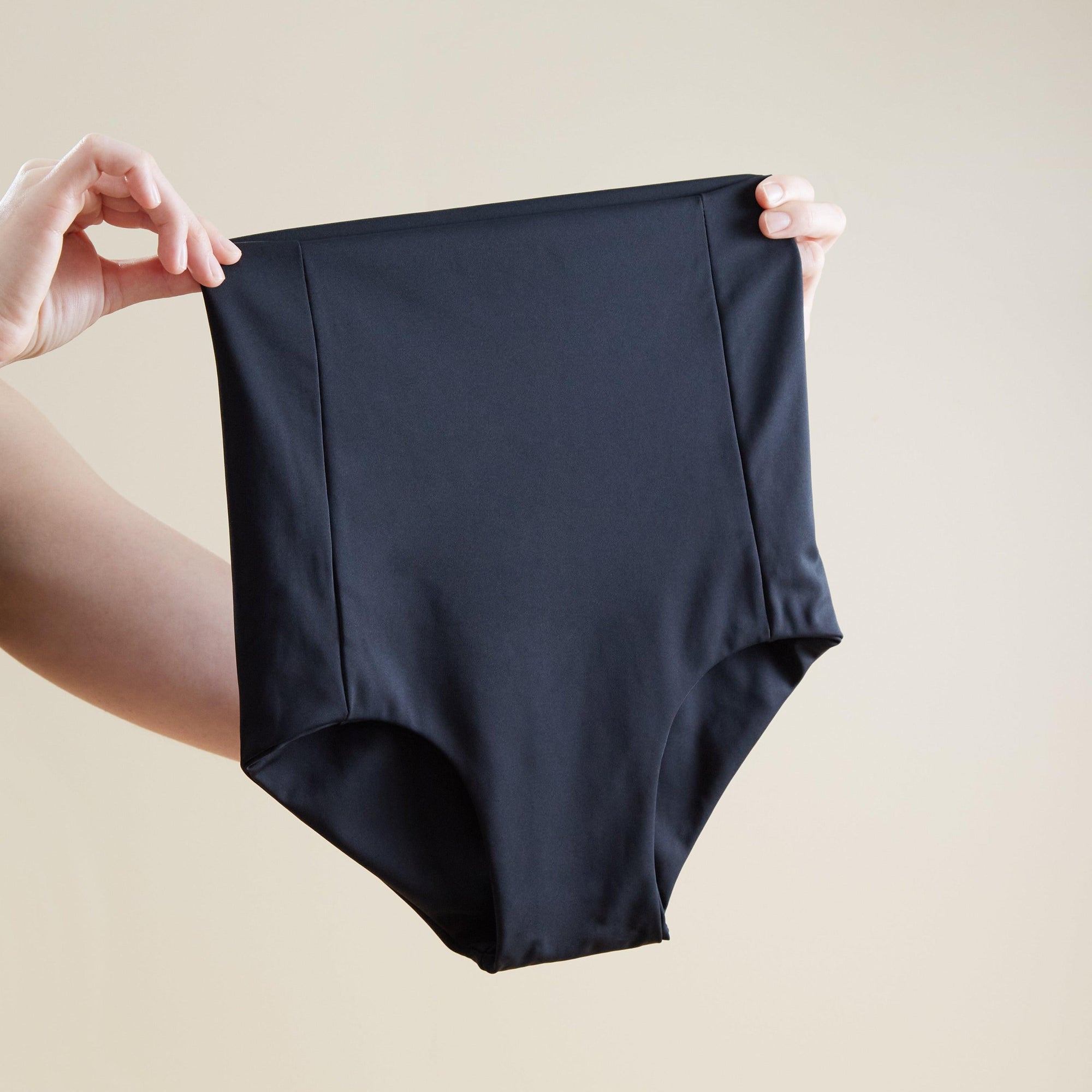 A woman showcasing Bare Mum brand's Postpartum Briefs on a beige background, promoting recovery after childbirth.