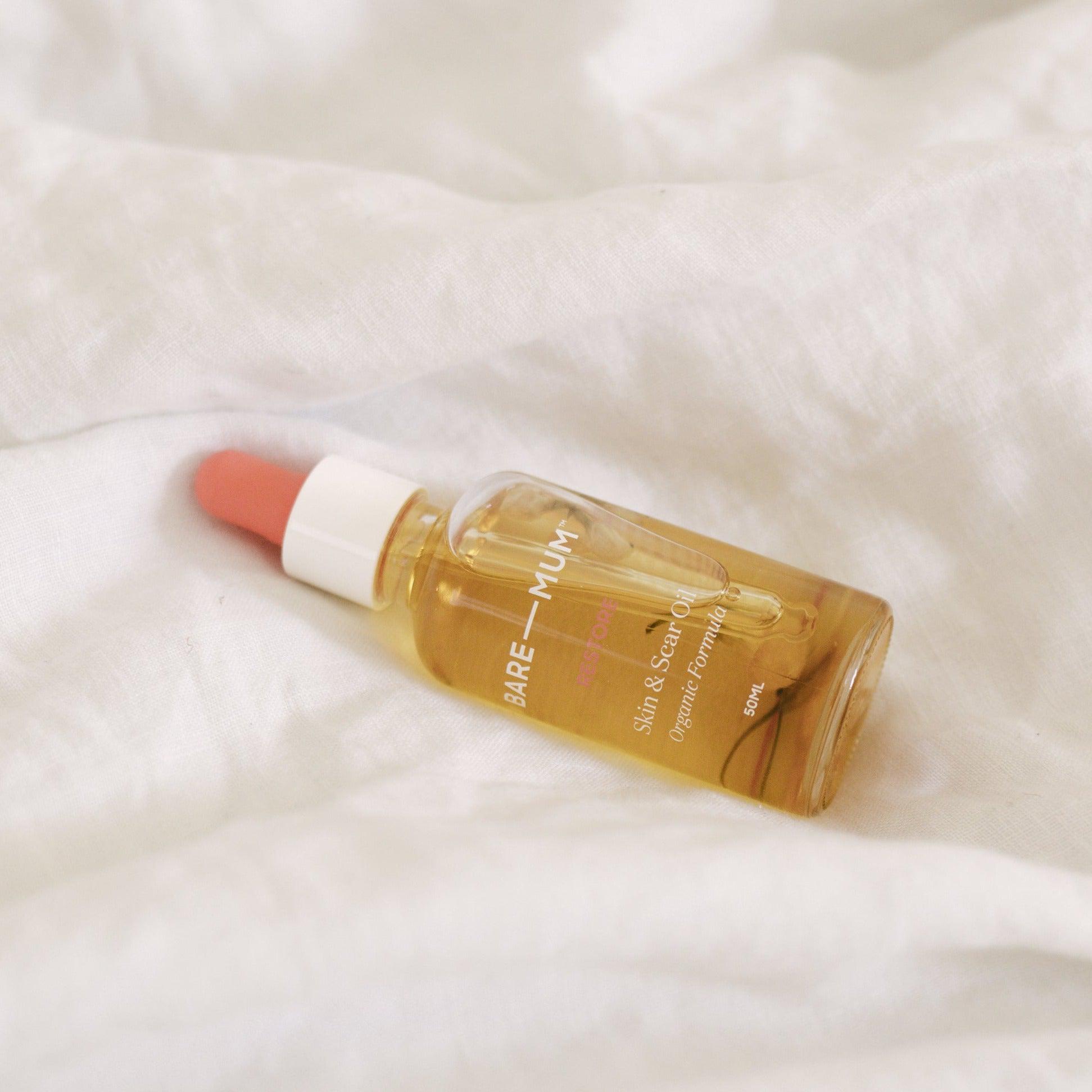 A small bottle of Bare Mum Skin & Scar Oil sitting on a white bed, perfect for postpartum recovery.