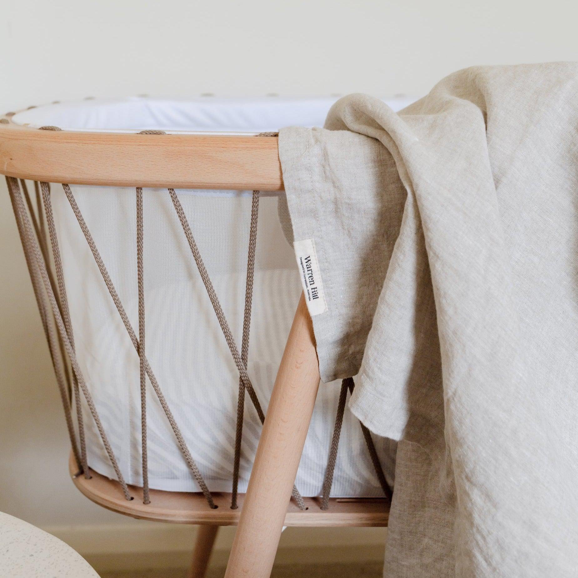 A Warren Hill crib with a french linen baby swaddle made of breathable stonewashed linen.