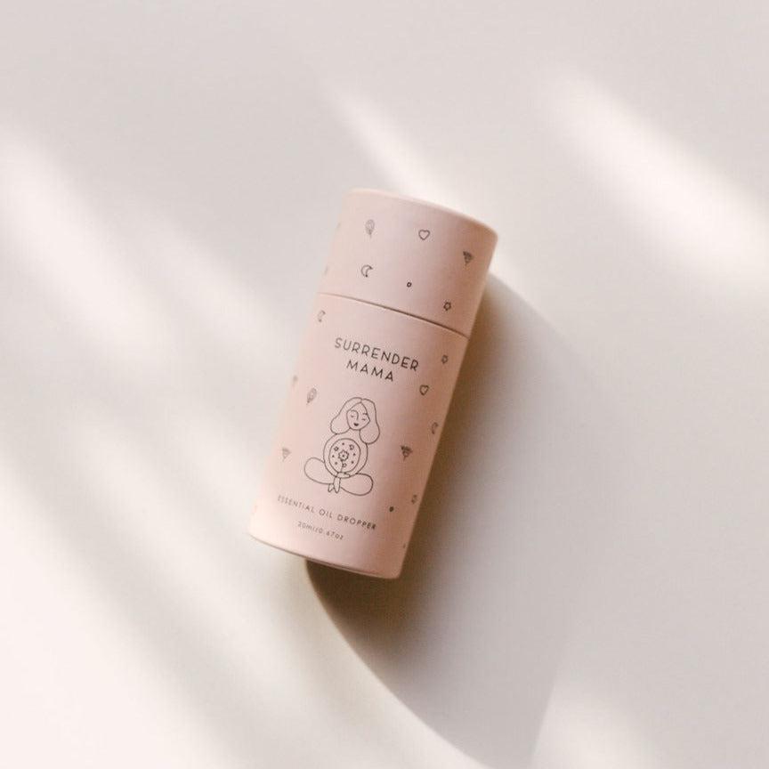 A Surrender Mama Essential Oil Dropper by Seasons of Mama, sitting on a white surface.
