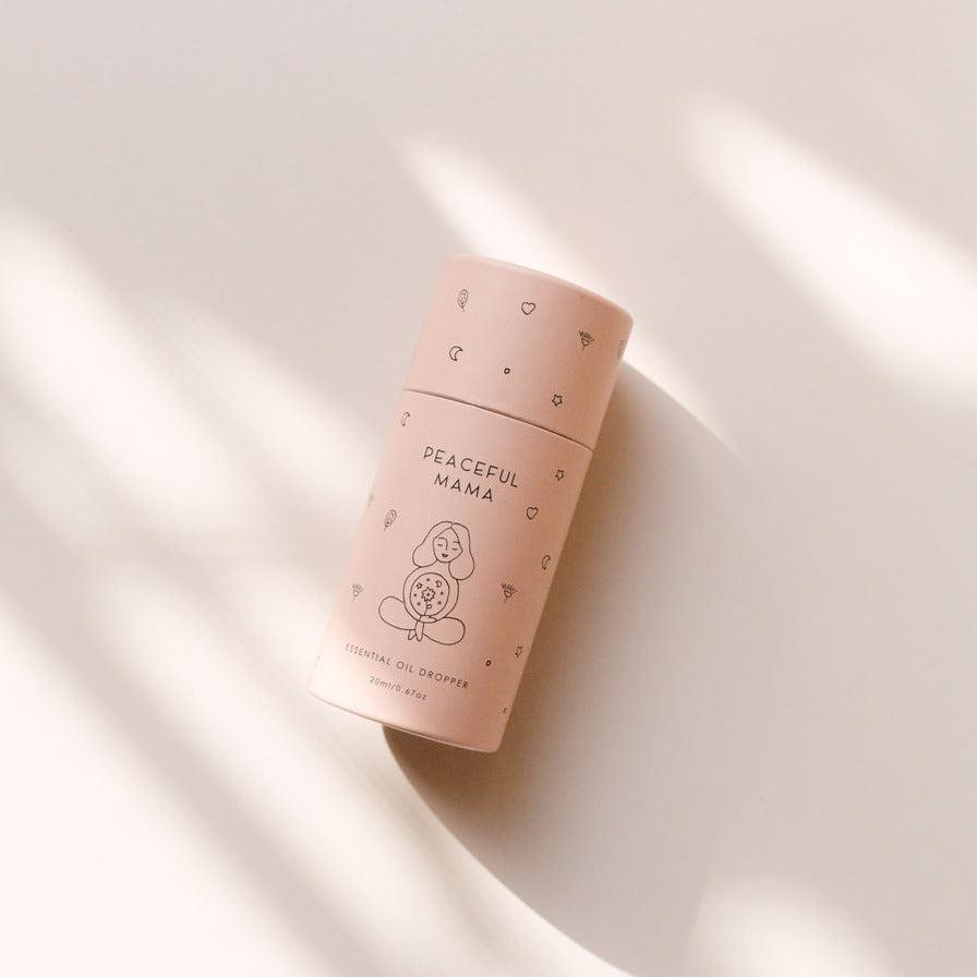 A bottle of Peaceful Mama Essential Oil Dropper from Seasons of Mama sitting on a white surface.