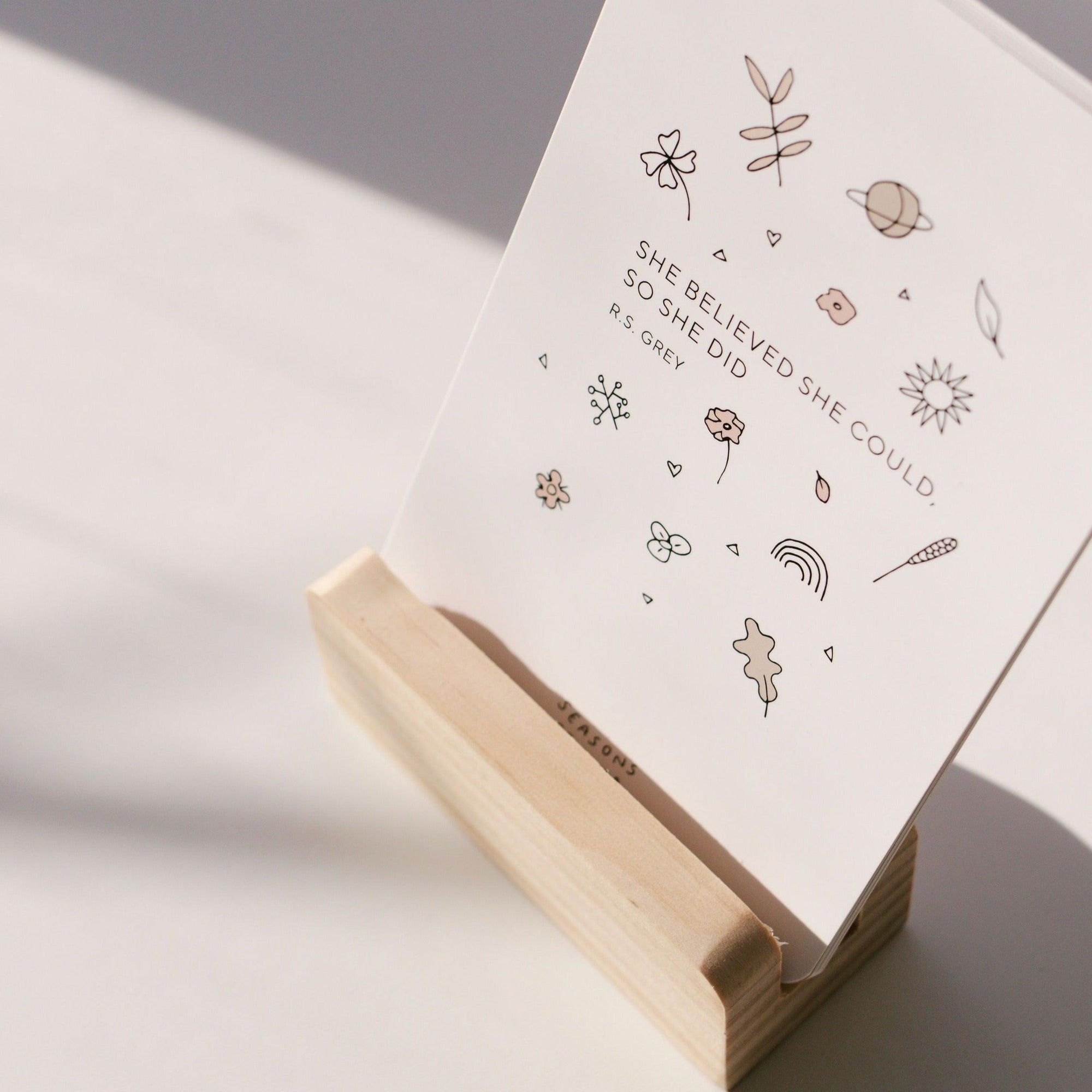 A wooden holder displaying a Seasons of Mama Birth Affirmation Card.