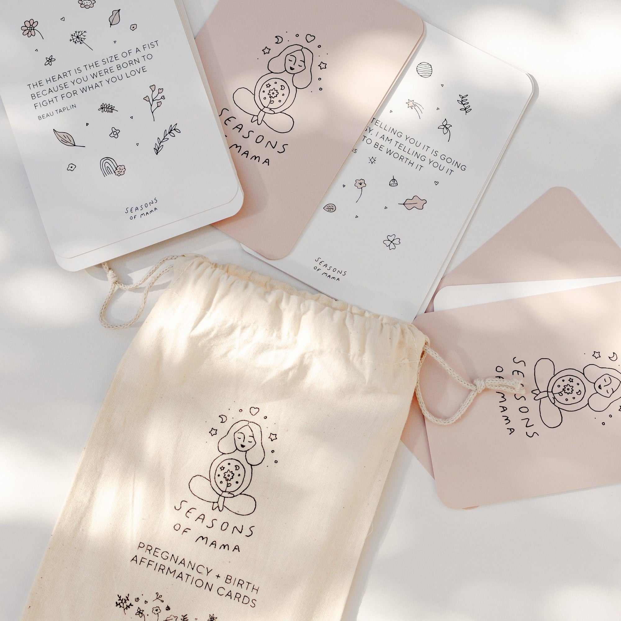 A table displaying a set of Seasons of Mama Birth Affirmation Cards and a Seasons of Mama branded calico bag bag.