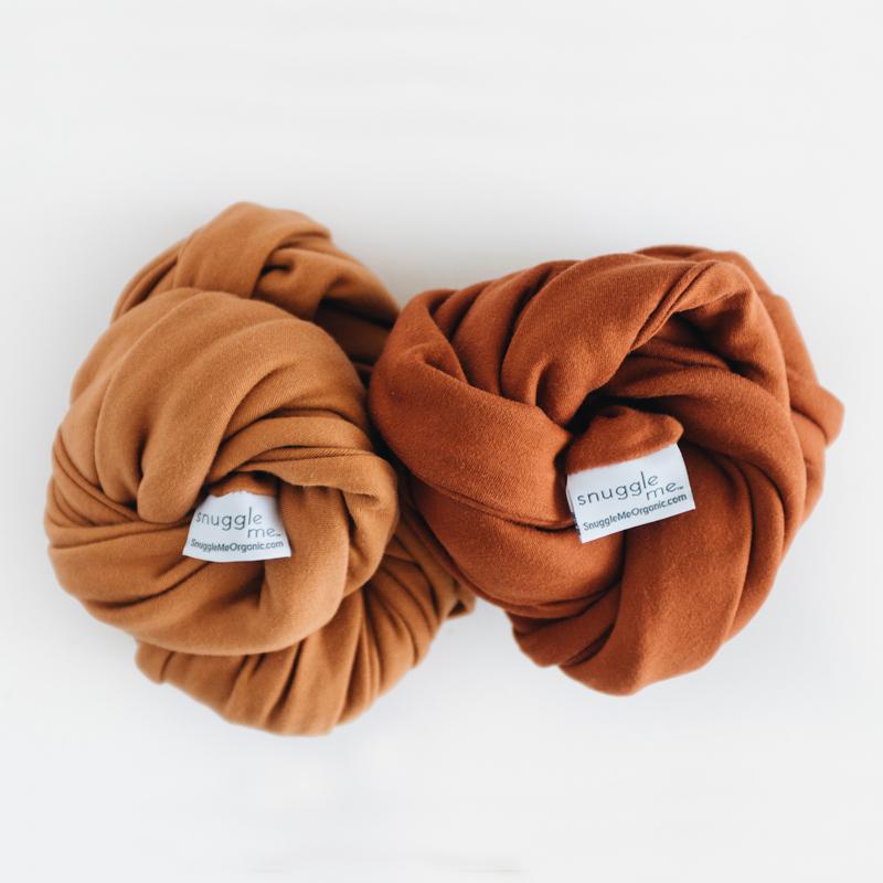Two Snuggle Me Lounger Covers rolled up on a white surface.
