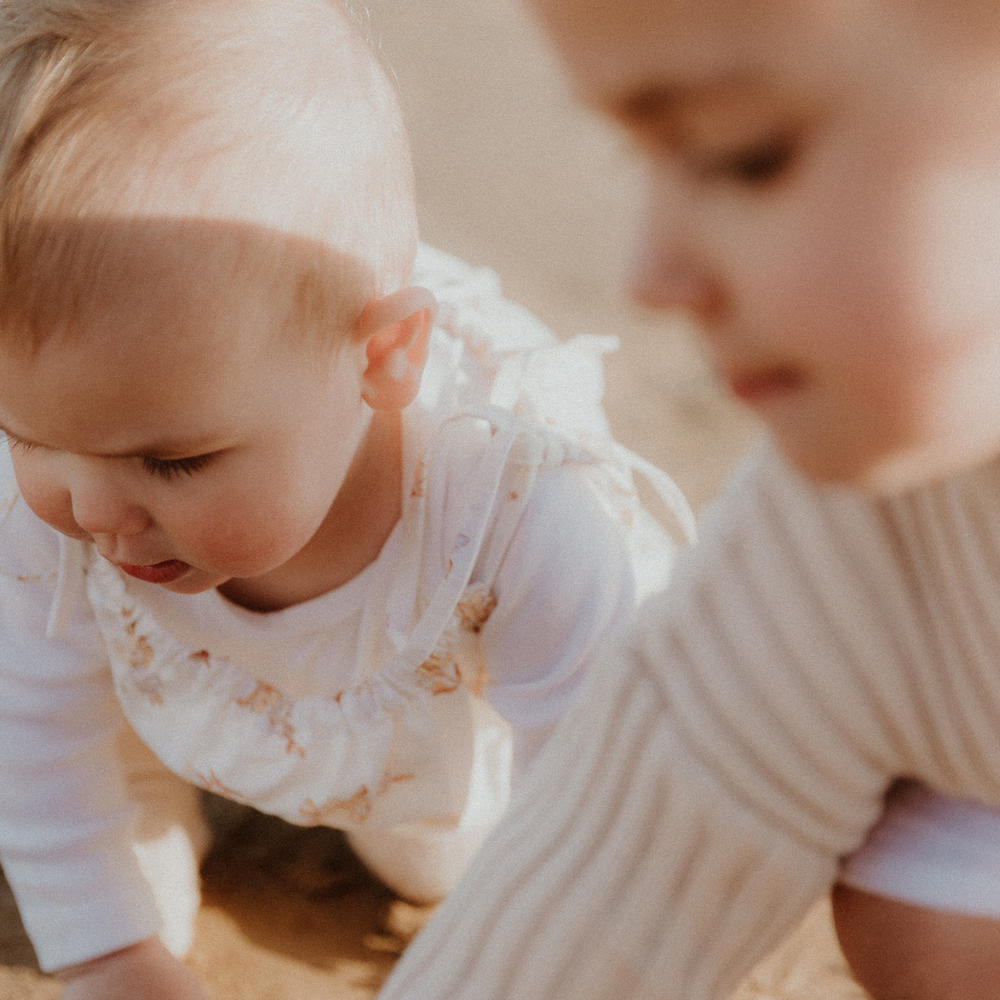 Two young children play on the sand at the beach together. They are new siblings learning to play with each other.
