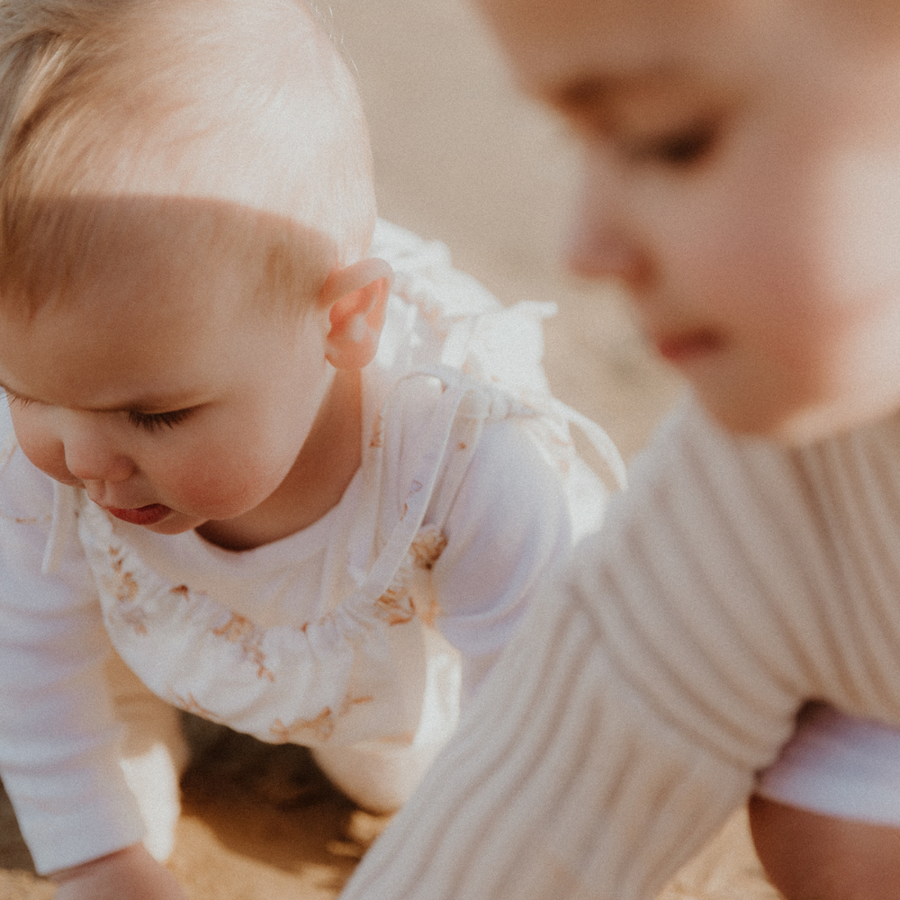 Two young children play on the sand at the beach together. They are new siblings learning to play with each other. 