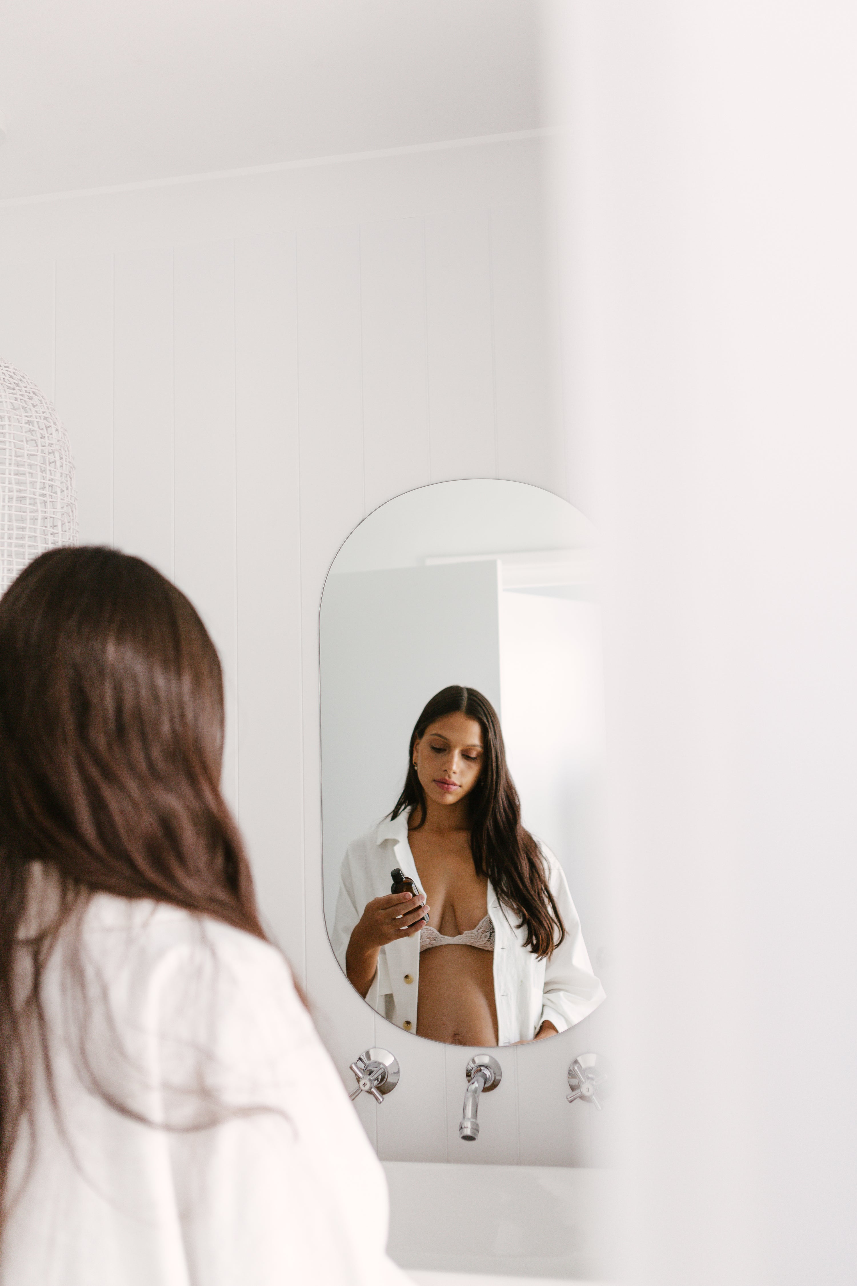 A woman in a white robe looking at herself in the mirror.