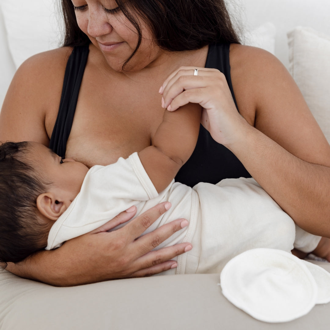 A woman is breastfeeding a baby in a knitted hat.