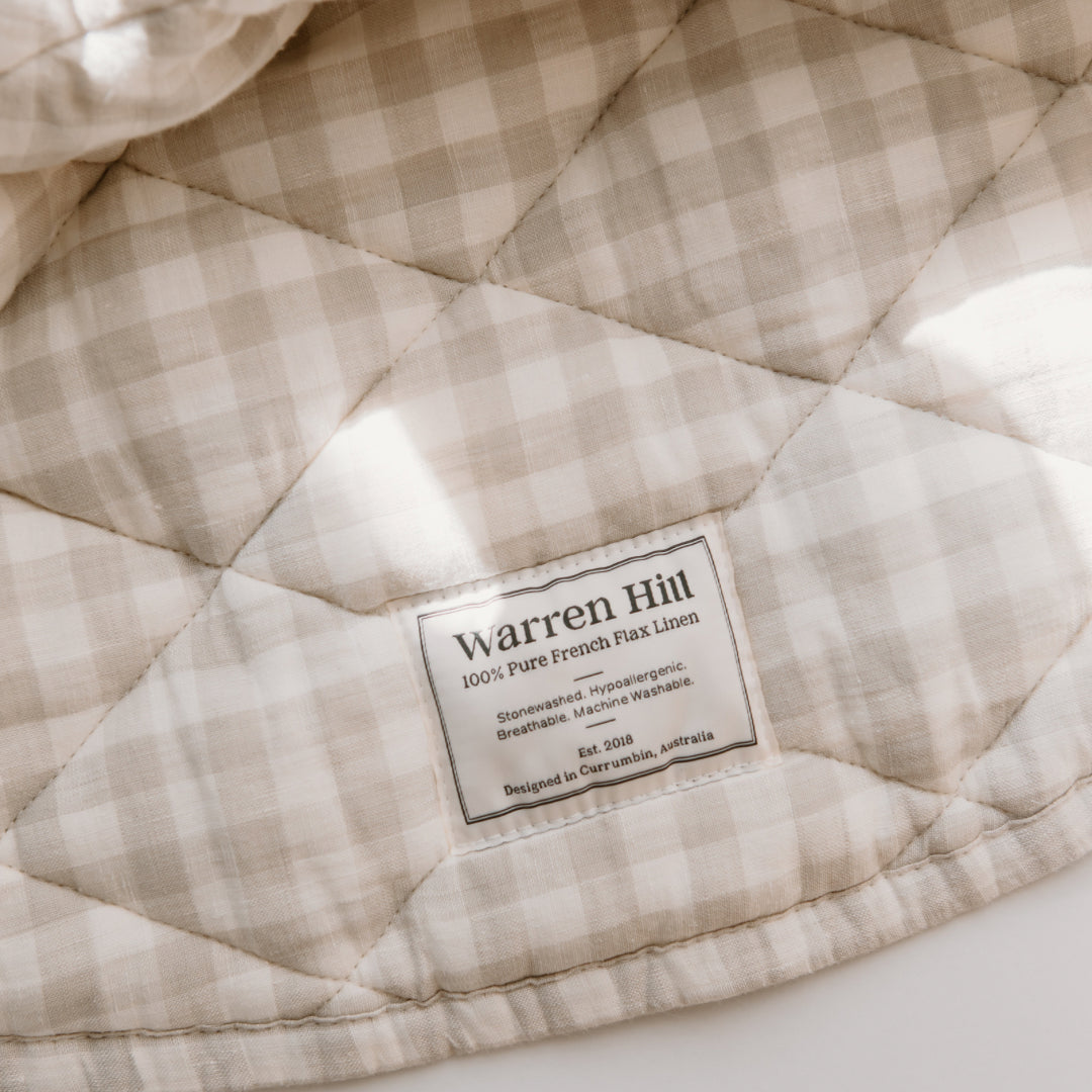Quilted blanket with a label indicating "warren hill play mat | gingham, 100% pure French Flax Linen," designed in Australia and hypoallergenic.