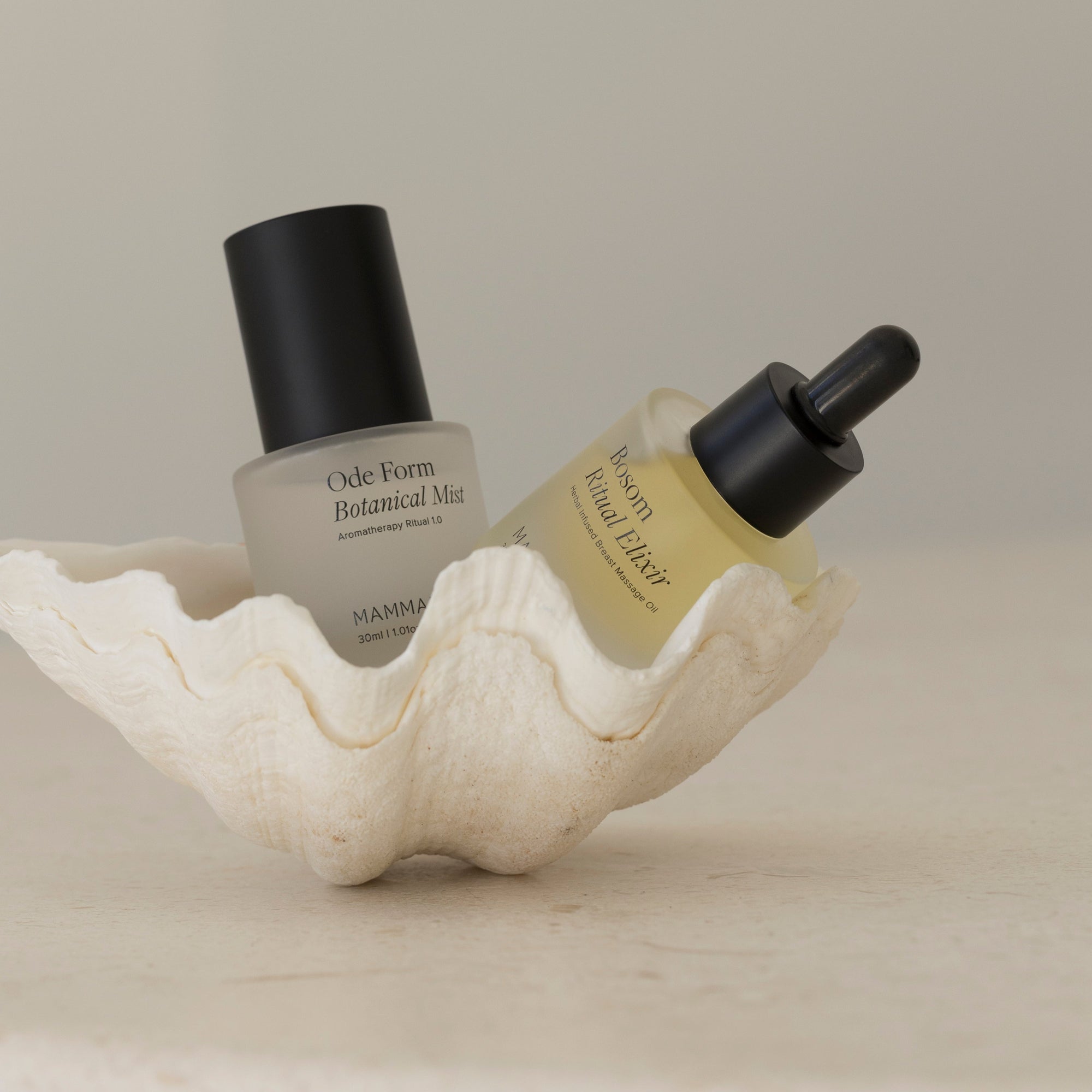 A bottle of Mammae EXCLUSIVE mini ode form botanical mist and a shell on a table.