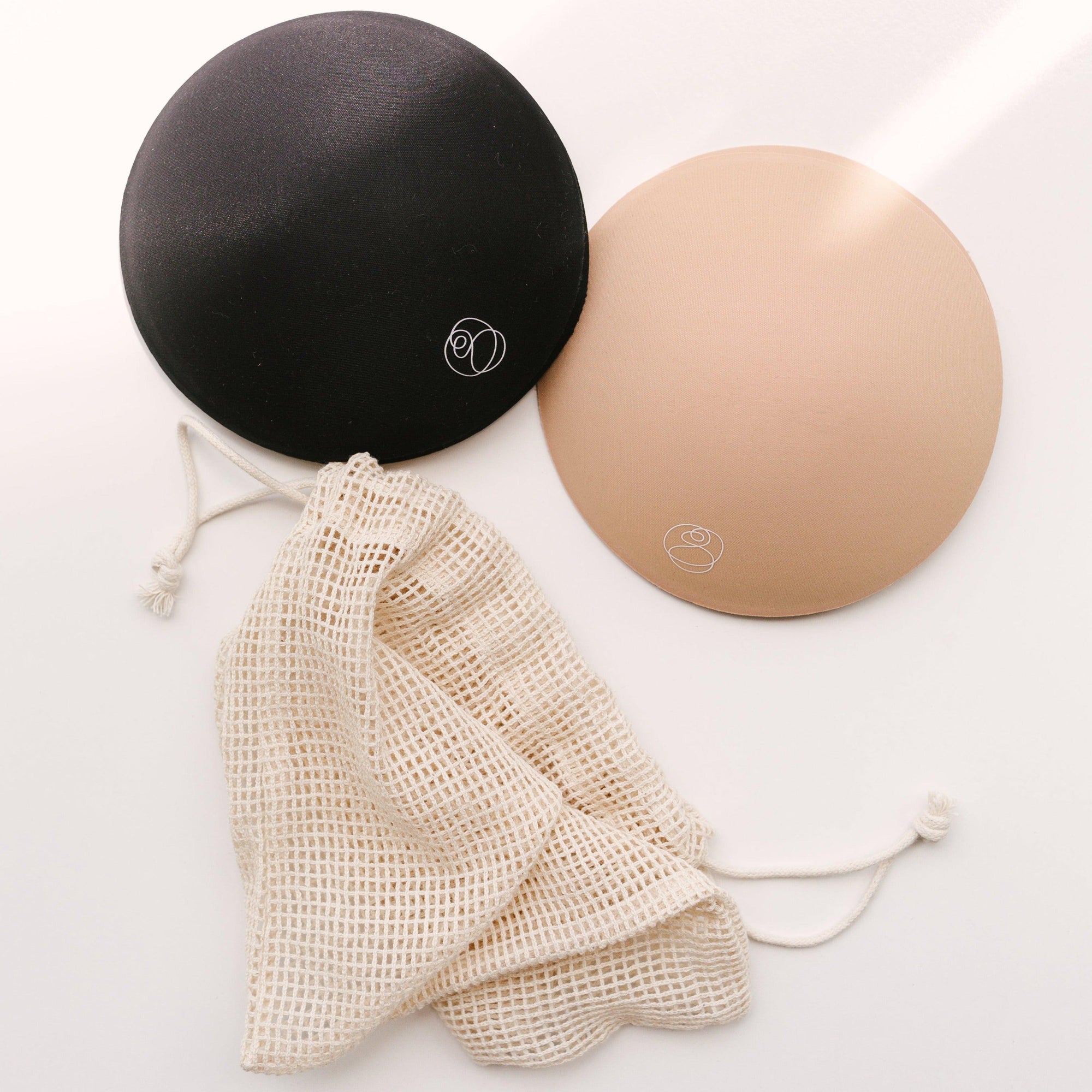 Two black and beige Bare Mum Breast Pads on a white surface.