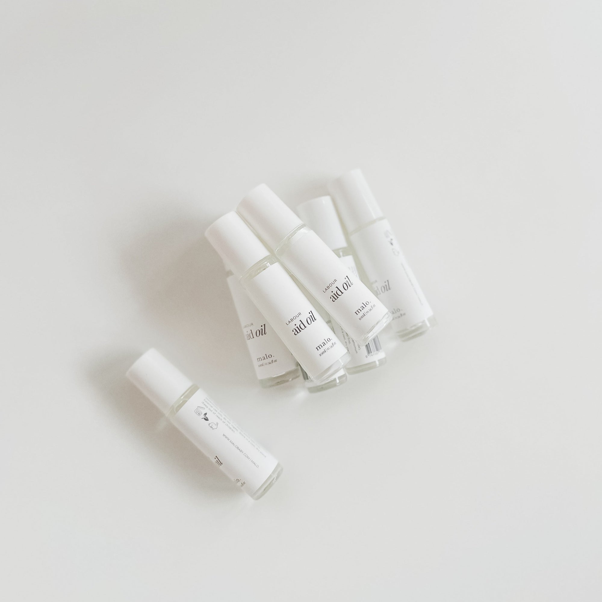 Five white nail polish bottles arranged on a plain background with Malo The Label's Cinnamon Bark Essential Oil.