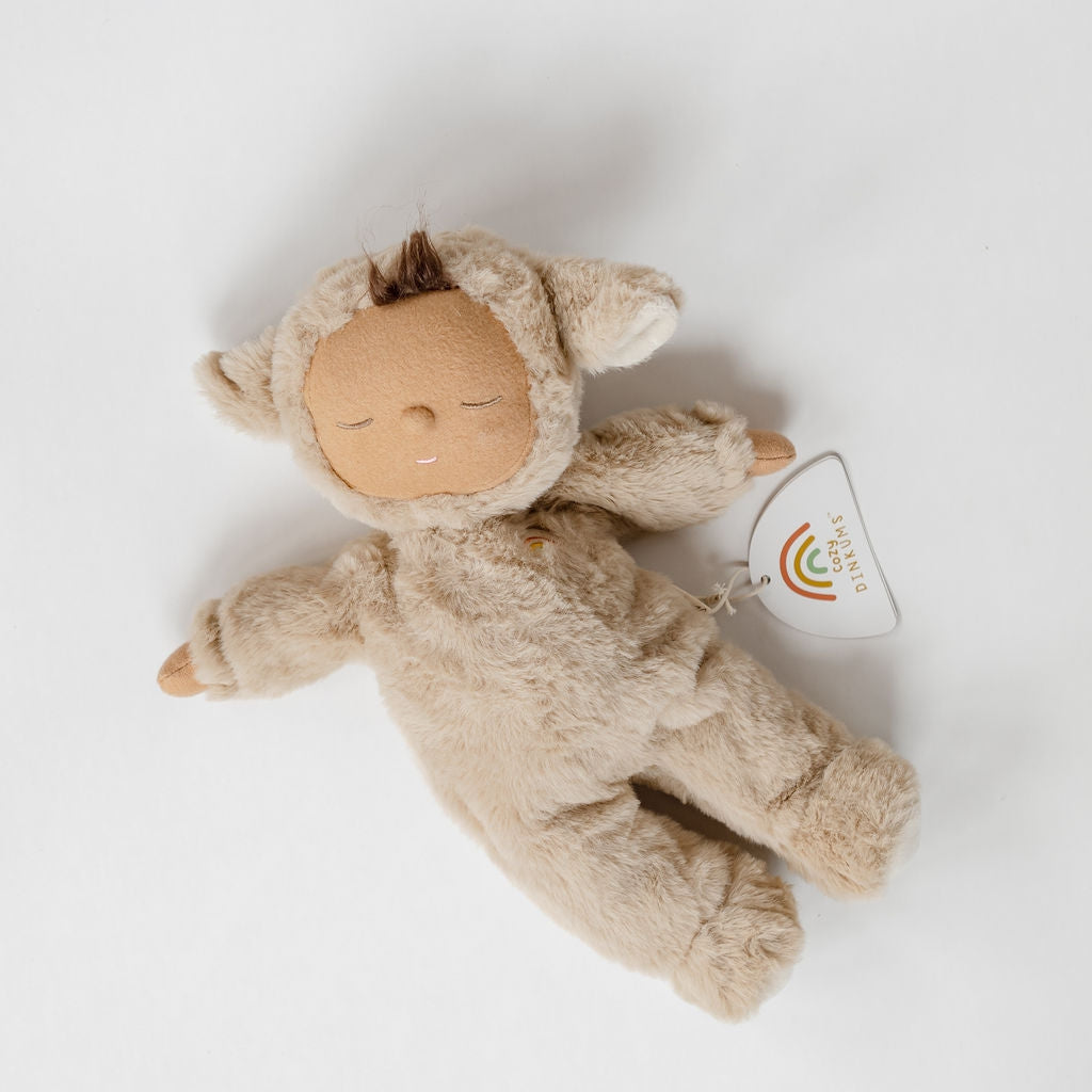 A beige Cozy Dinkums stuffed animal lying on a white surface.