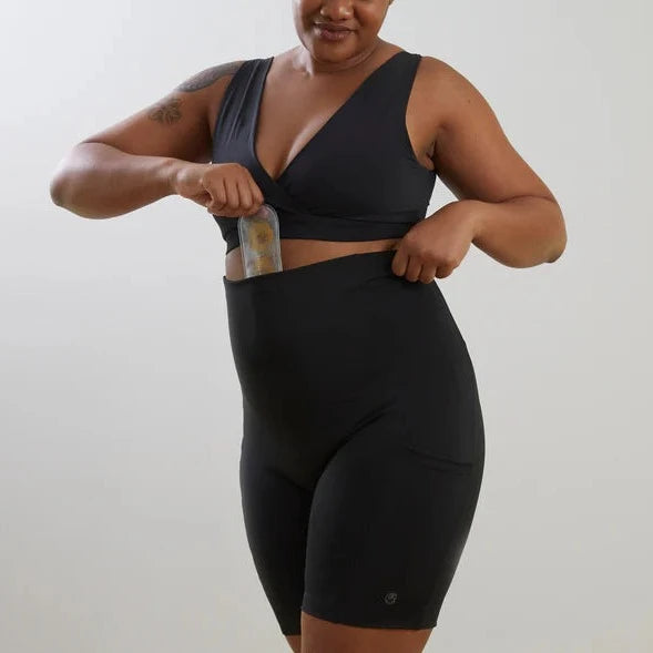 A woman in a black workout outfit featuring Bare Mum Postpartum Recovery Shorts, holding a resistance band, and showcasing the garment's pocket feature.