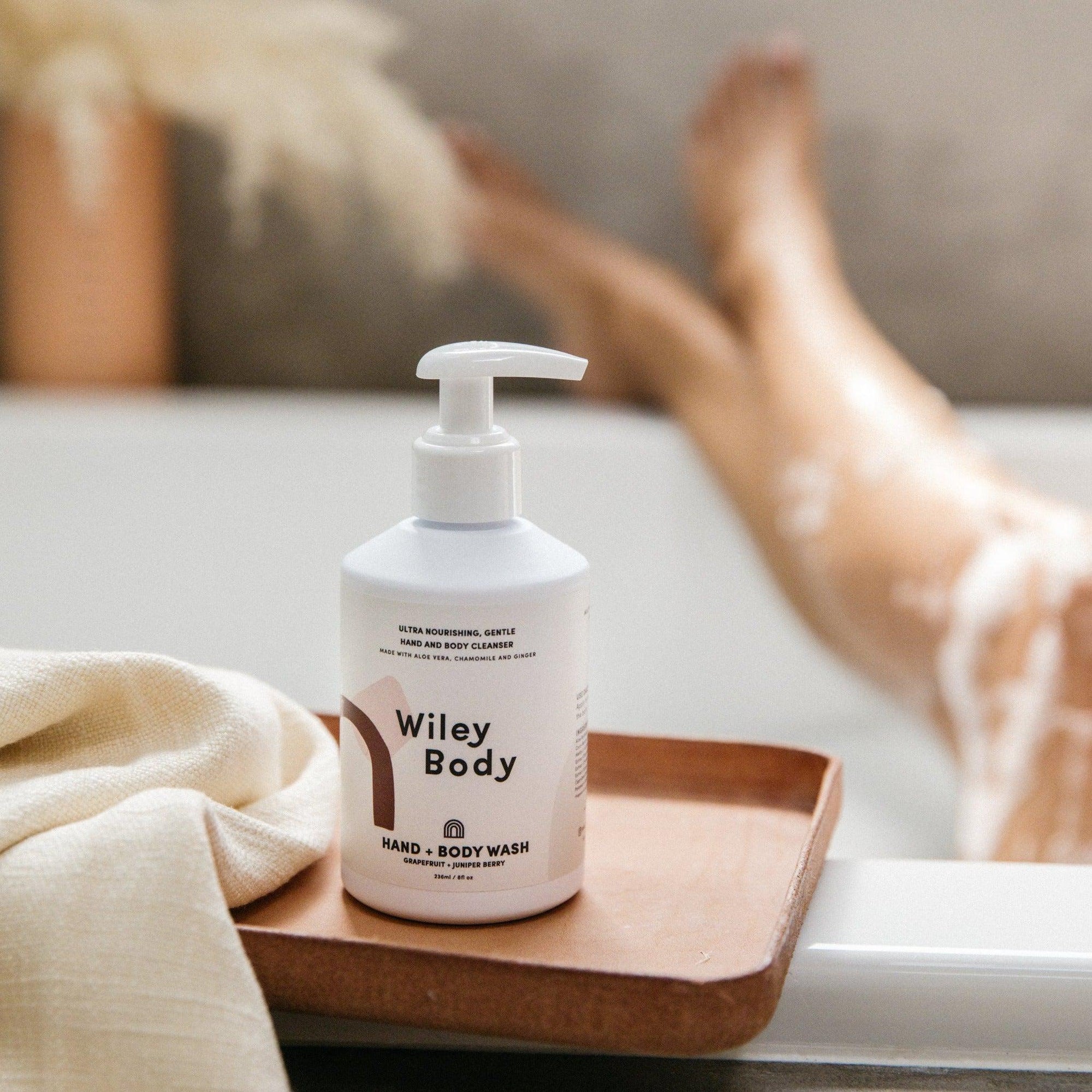 A bottle of Wiley Body hand & body wash sitting on a tray next to a woman's legs.