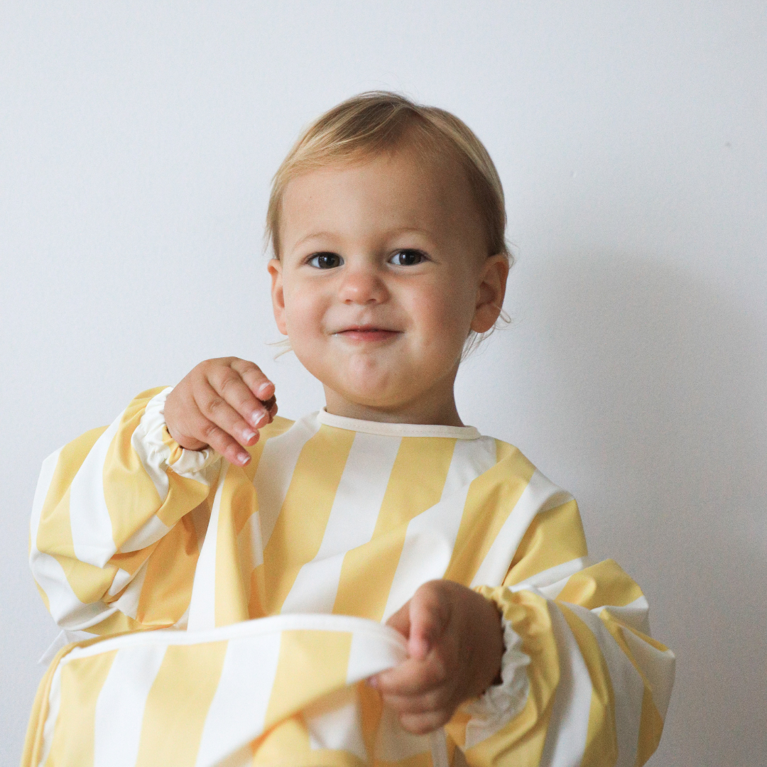 A child wearing a Rommer Smock Bib in a super soft fabric with striped colour variations.