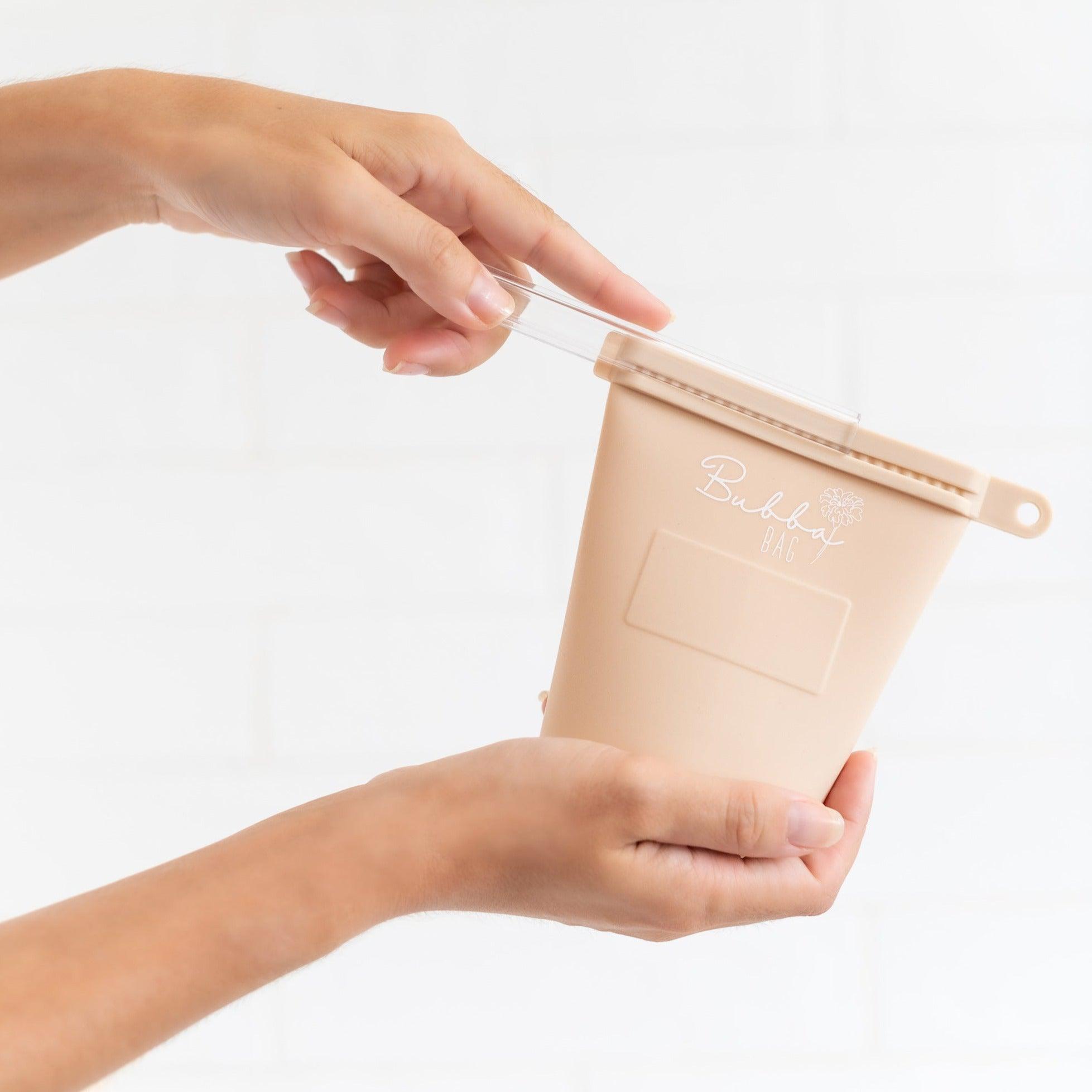A person holding a Marigold Baby bubba bags | mocha, a reusable beige plastic container with a lid for breast milk storage.