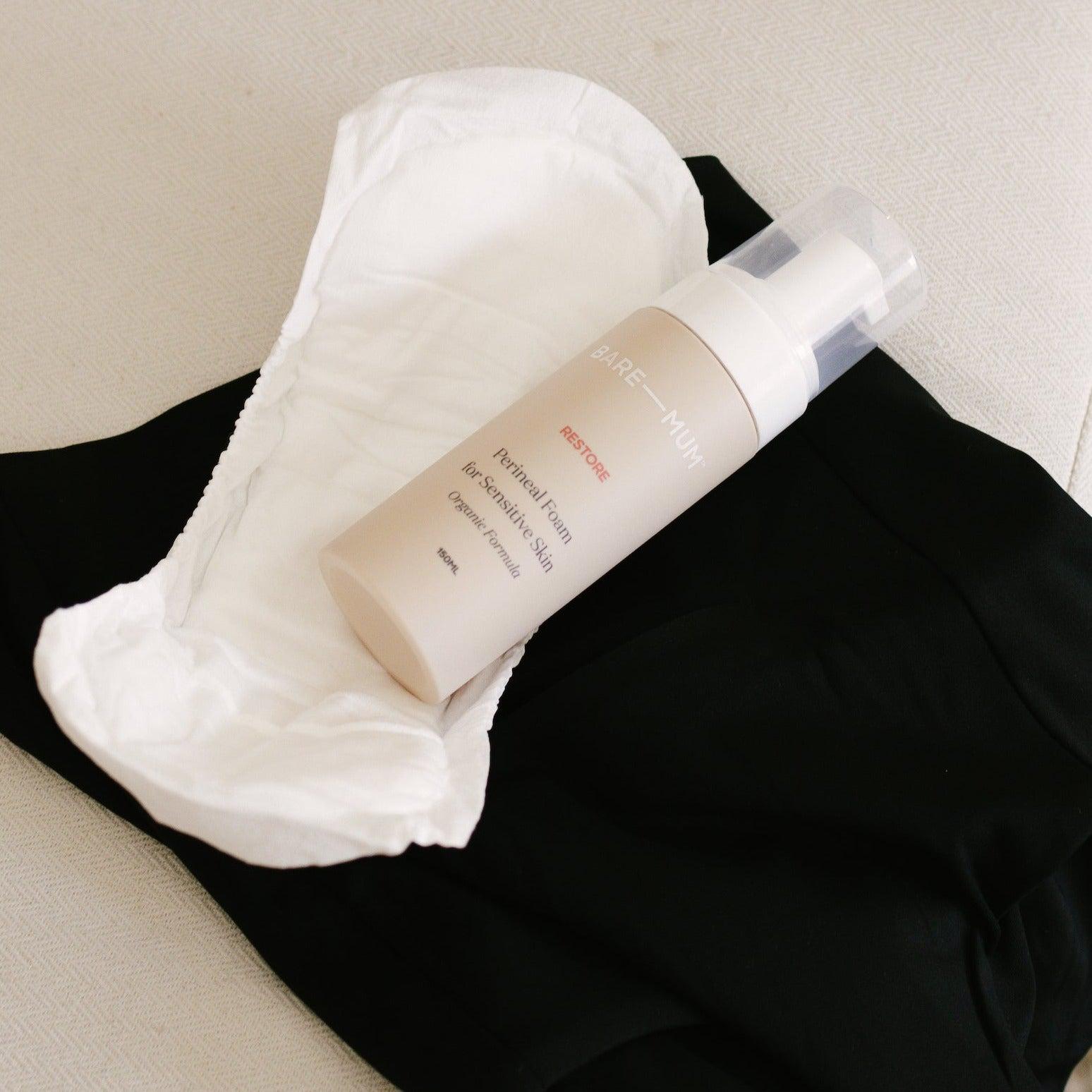 A breastfeeding mother's bottle of Bare Mum Perineal Foam sitting on top of a pair of black postpartum briefs..