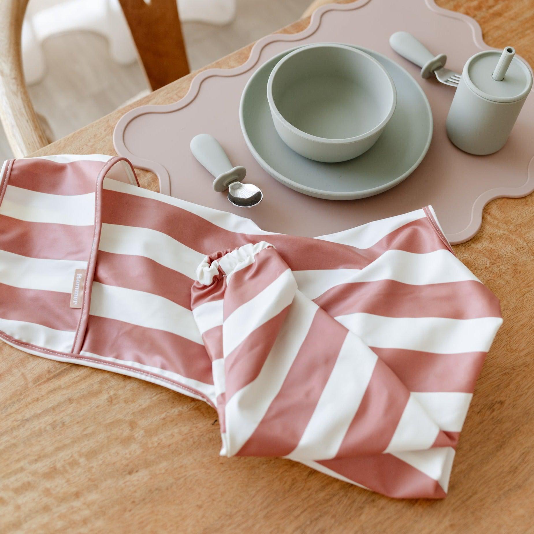 A Rommer Smock Bib in cinnamon on a table, featuring striped colour variations.