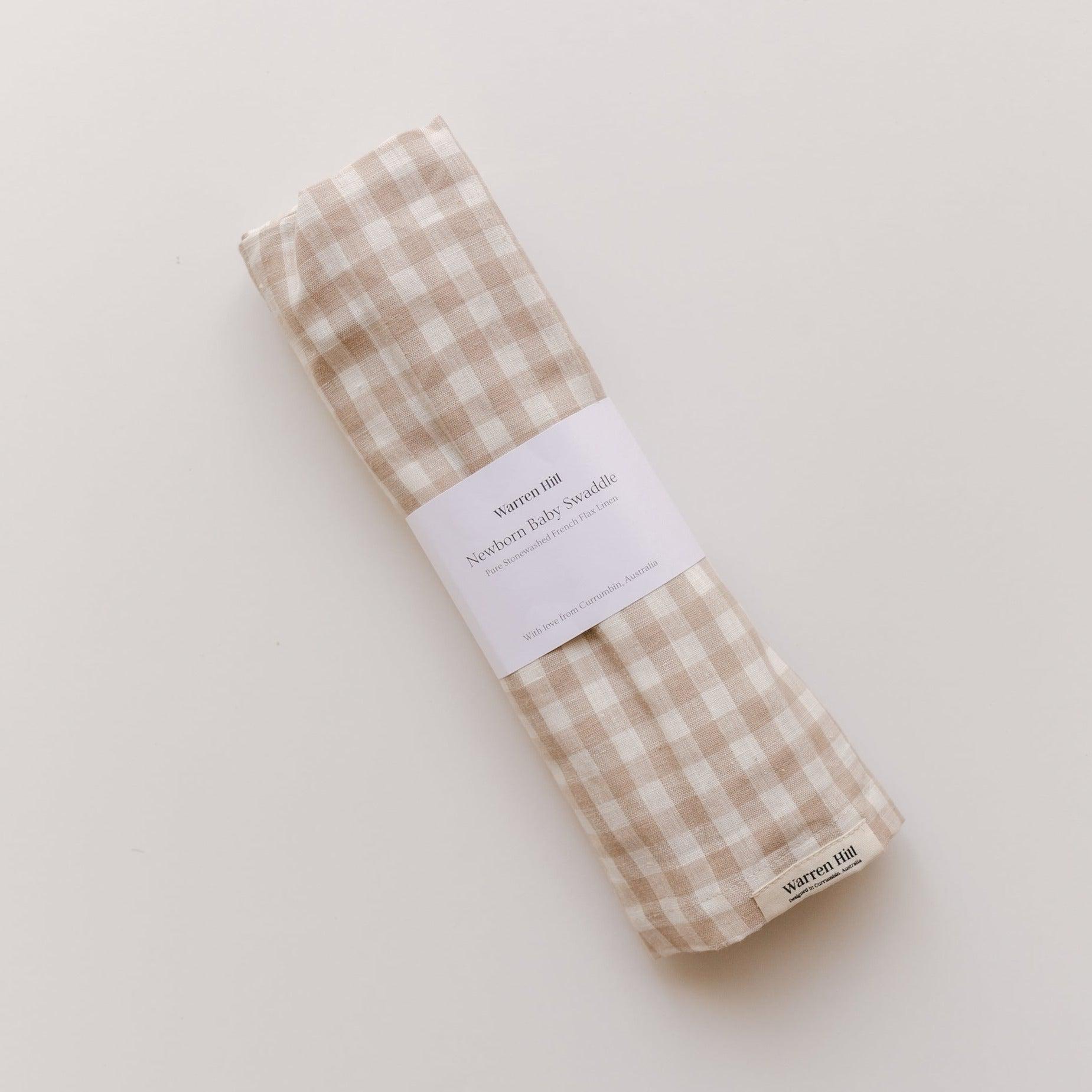 A beige and white gingham Warren Hill French linen napkin on a white surface.