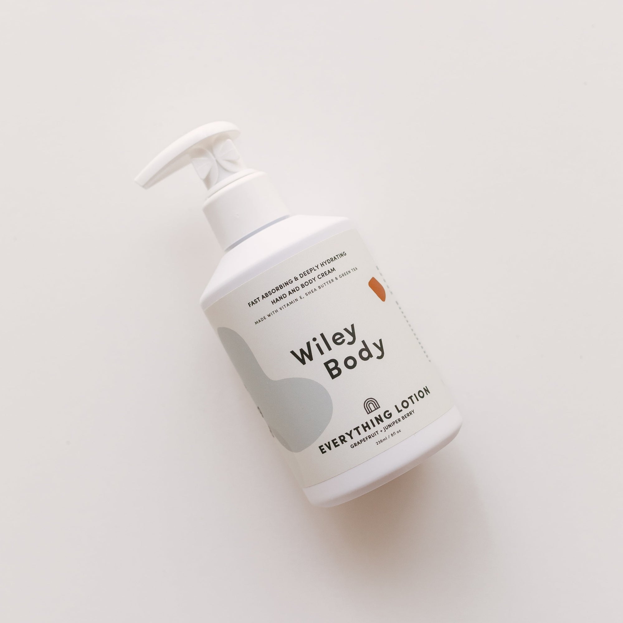 A lightweight bottle of Wiley Body's everything lotion, designed to hydrate and improve skincare, resting on a white surface.