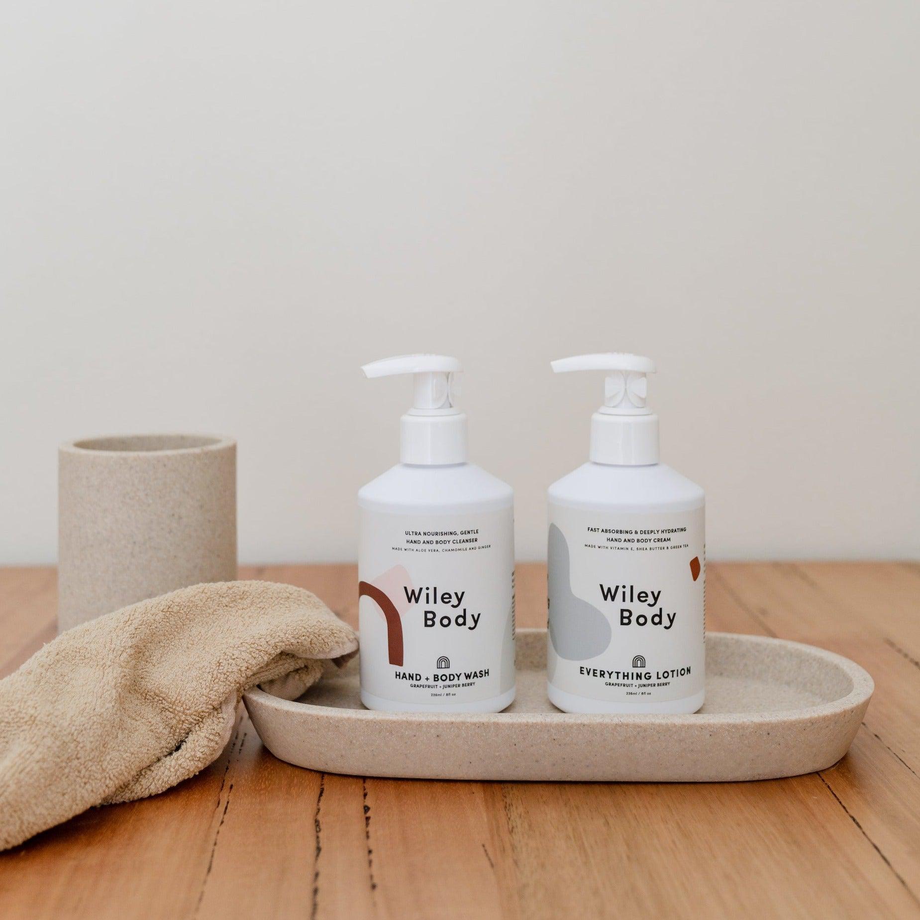 A lightweight bottle of Wiley Body's everything lotion and a towel on a wooden tray.