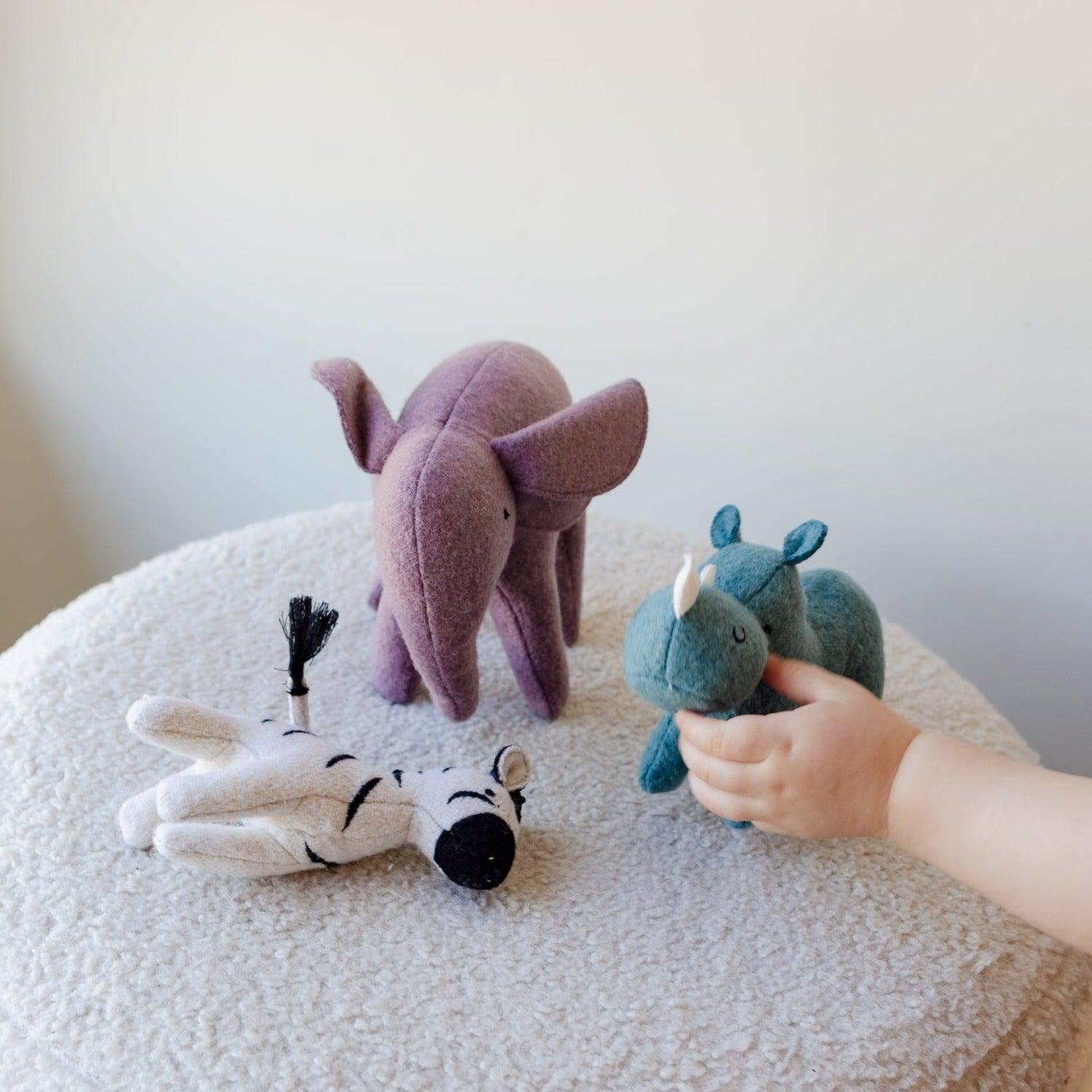 A child is playing with Olli Ella's Holdie Folk - Safari Animals on top of a table made from a wool blend fabric.
