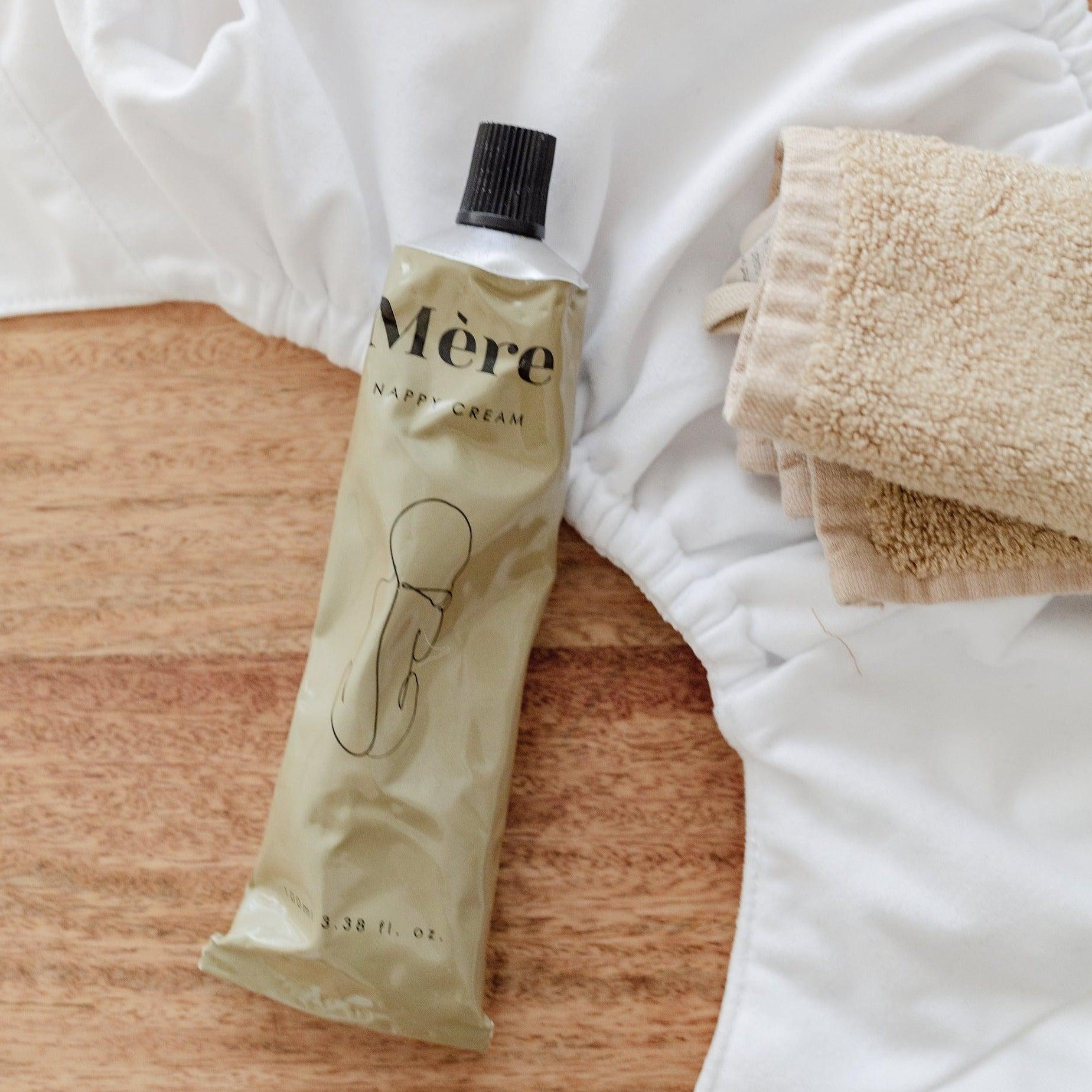 A tube of Mère Nappy Cream and a towel on a wooden table.