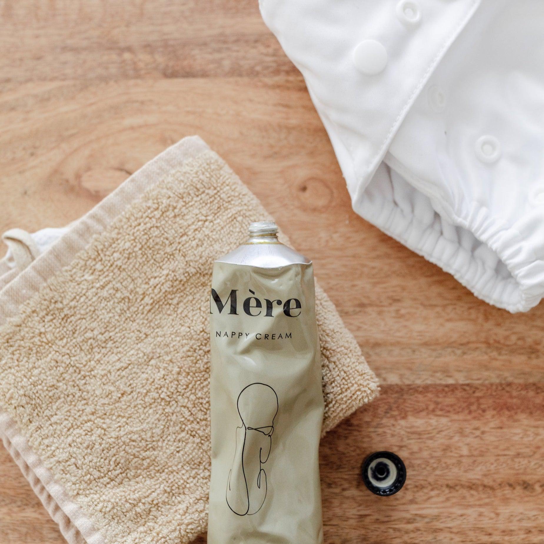 A tube of Mère Nappy Cream and a towel on a wooden table.