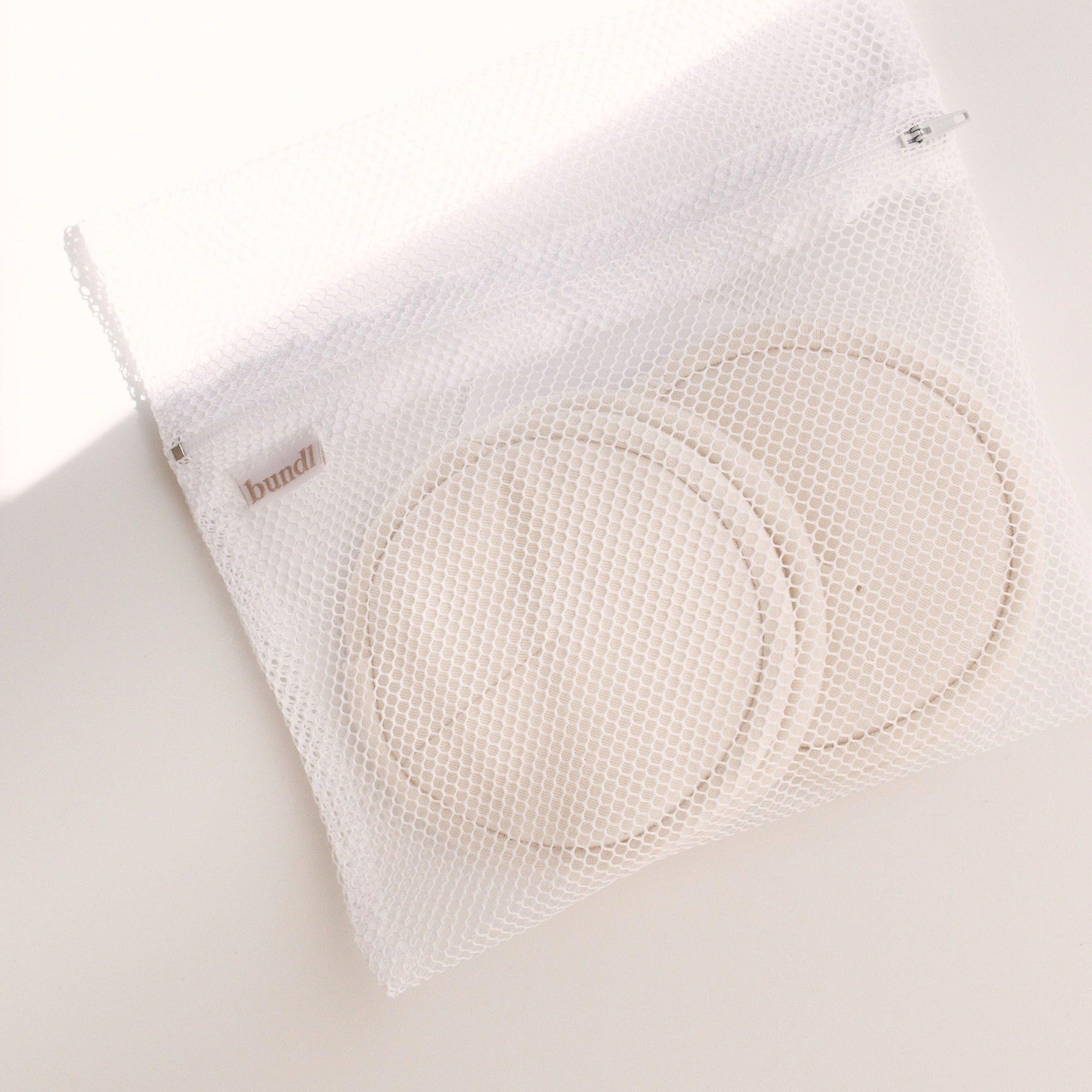 A Bundl. white mesh bag with two Bundl. breast pads.