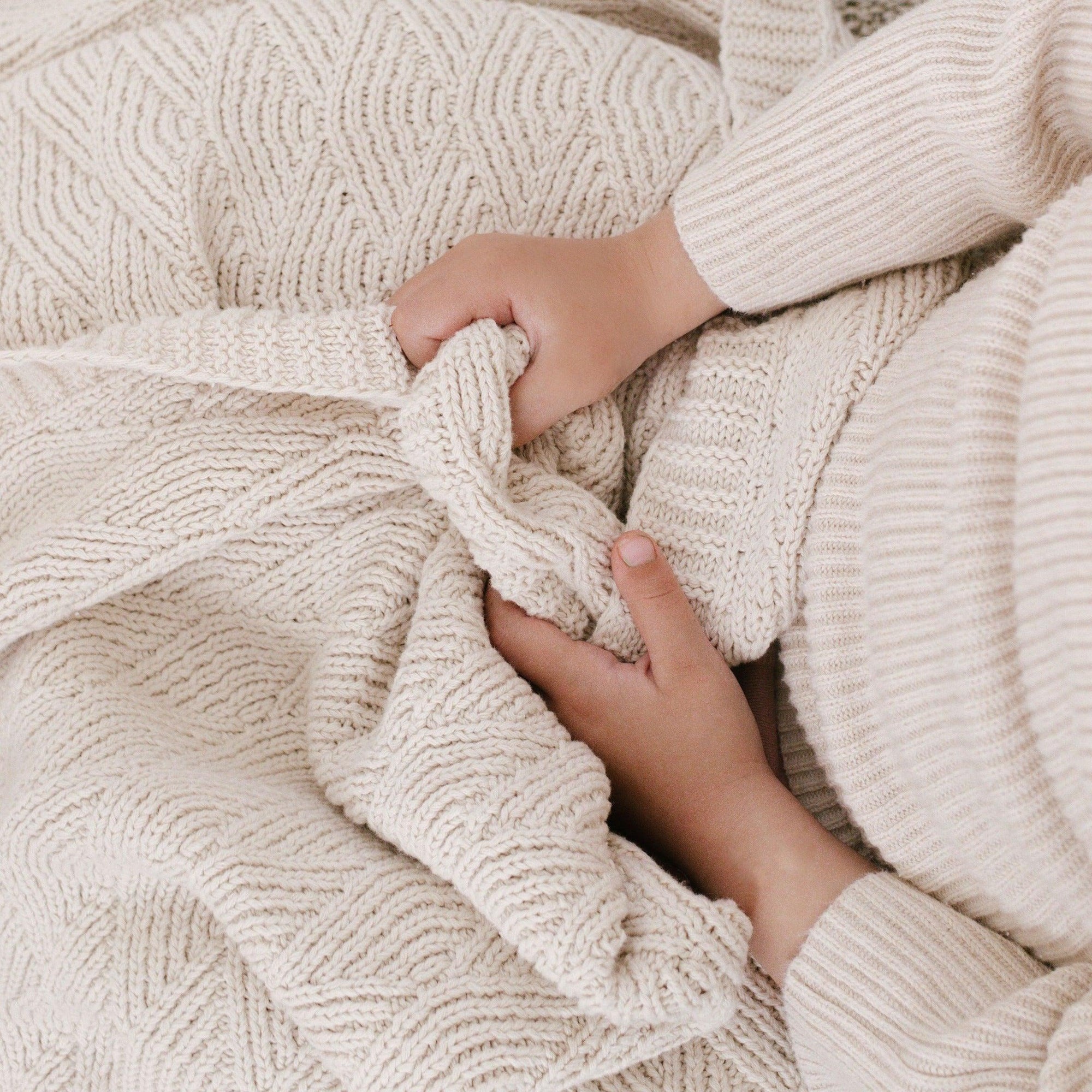 A person holding a Bundl. knitted organic cotton blanket on a bed.