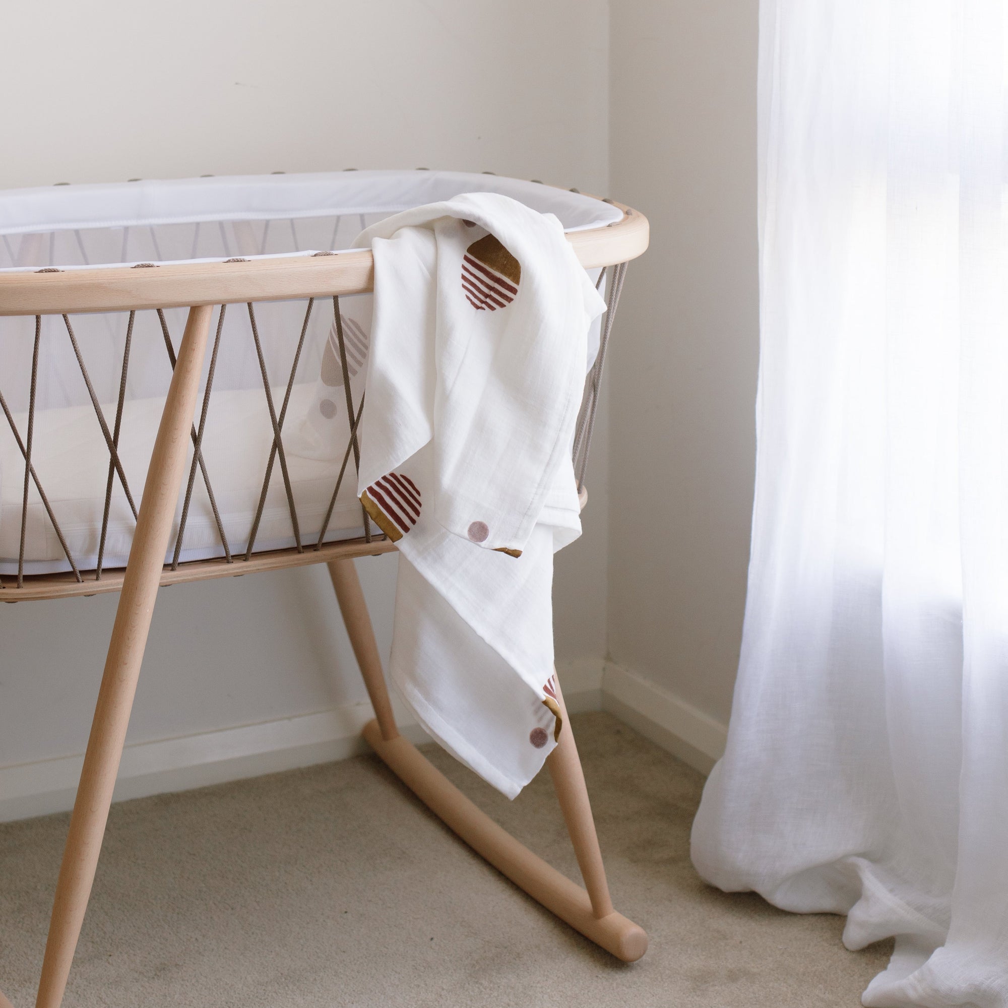 A Charlie Crane KUMI bassinet in Hazelnut in a room draped with a blanket.
