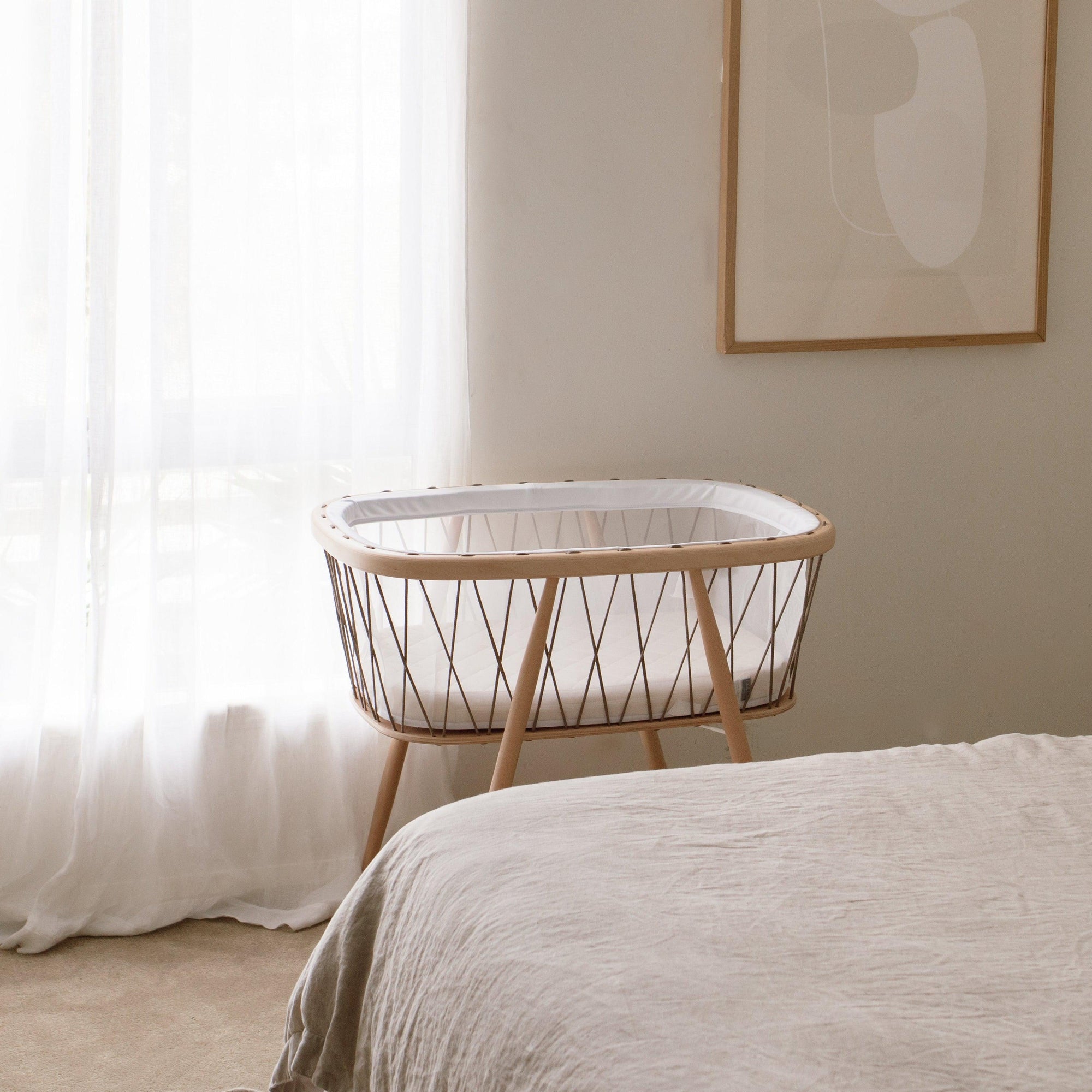 A KUMI bassinet in hazelnut colour by Charlie Crane next to a bed.
