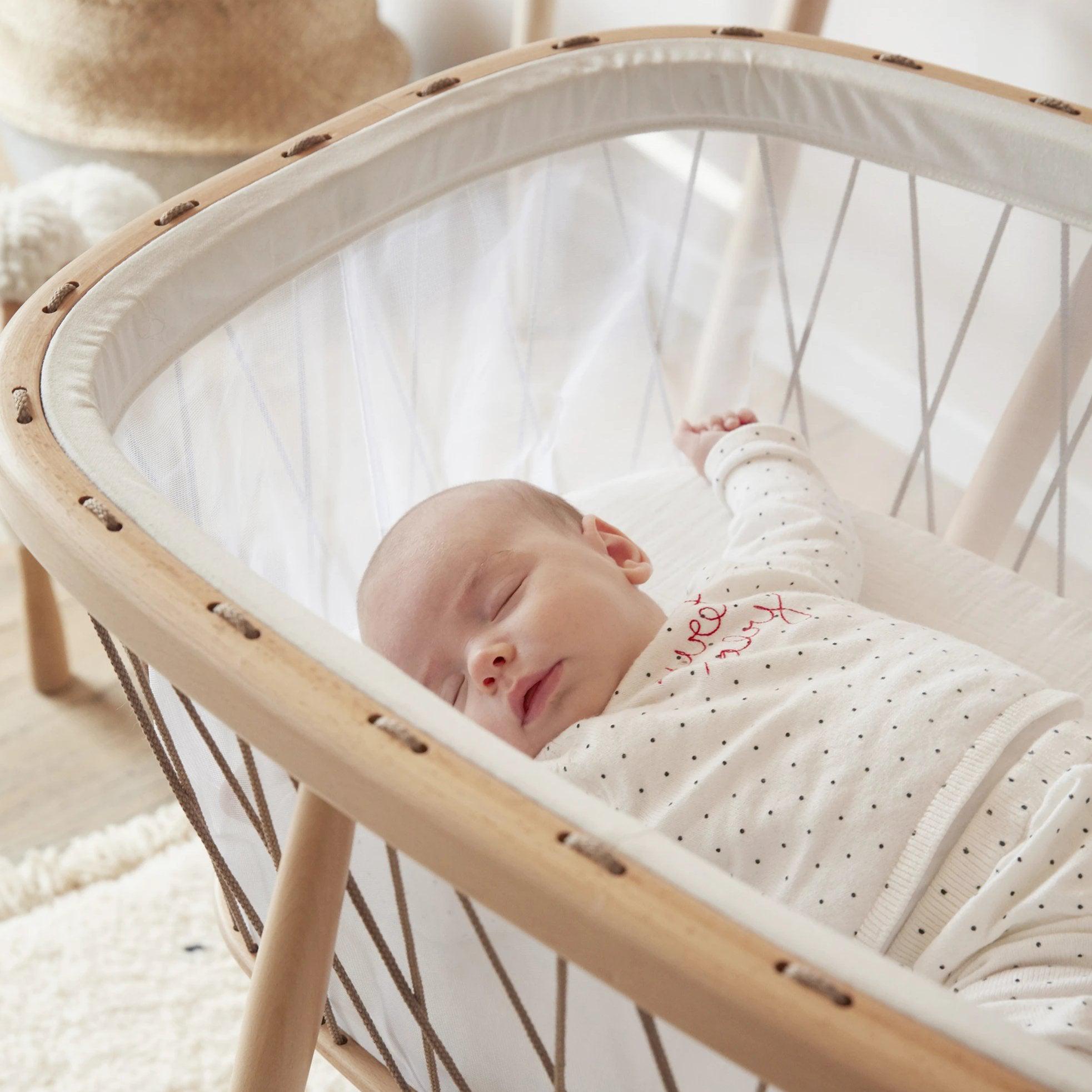 A Charlie Crane KUMI bassinet in Hazelnut with a baby sleeping in it.