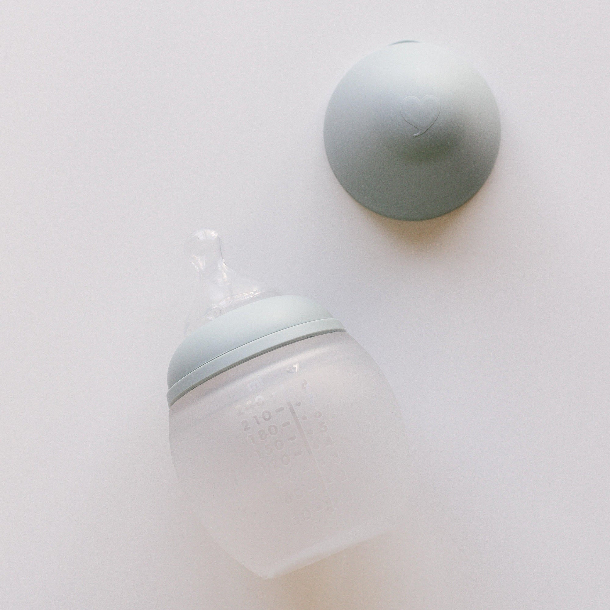 An Elhée France BibRond ivy green baby bottle on a white surface.