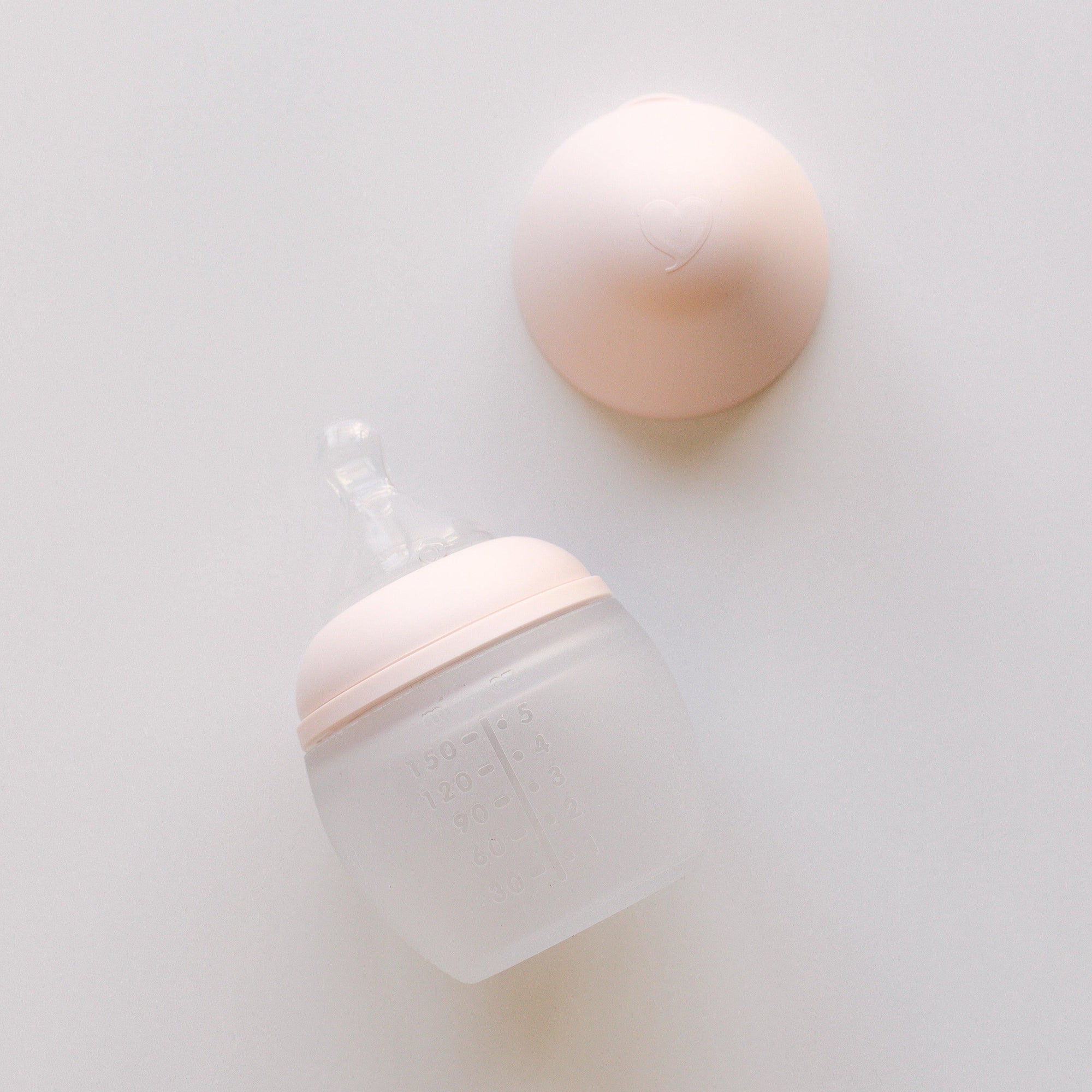 An Elhée France BibRond nude baby bottle laying on a white surface.