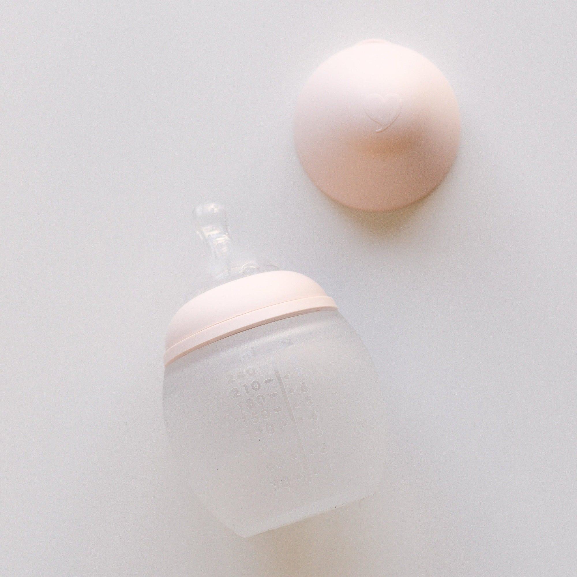 An Elhée France BibRond nude baby bottle laying on a white surface.