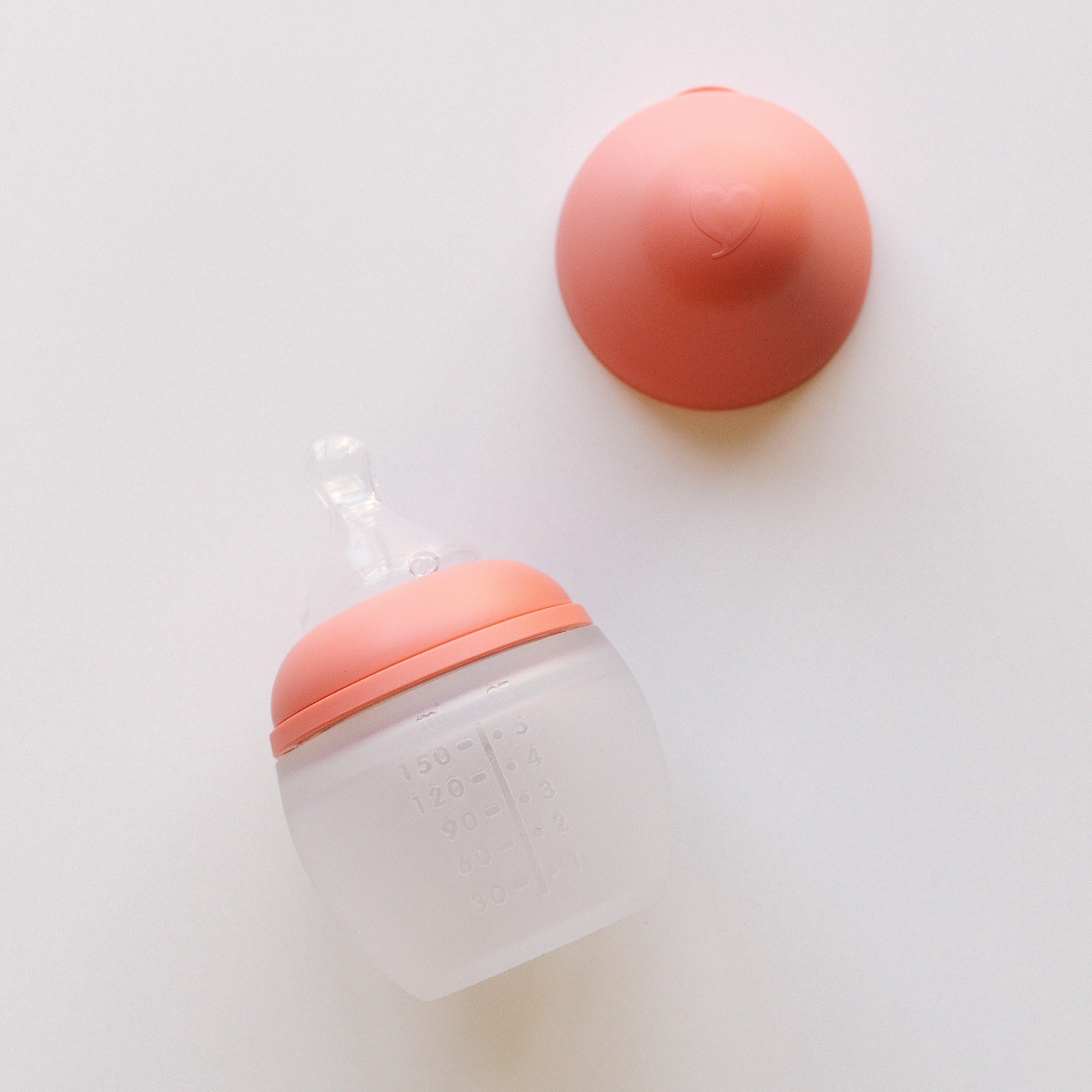 A BibRond summer coral baby bottle by Elhée France laying on a white surface.